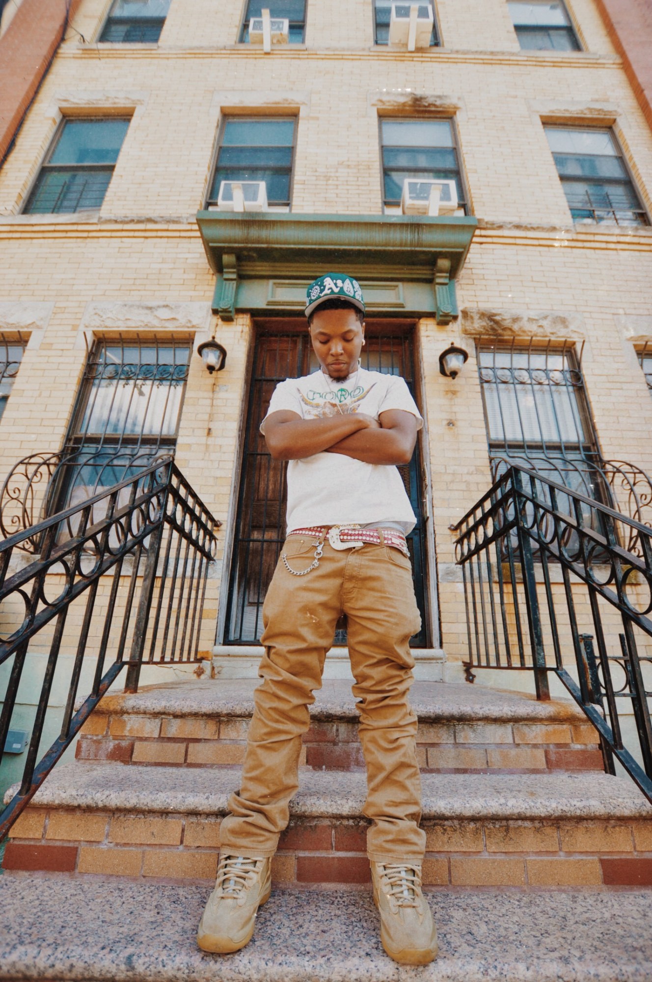 a portrait of artist jasiah wearing a white graphic t and stone jeans. he has his arm crossed on a doorstep.