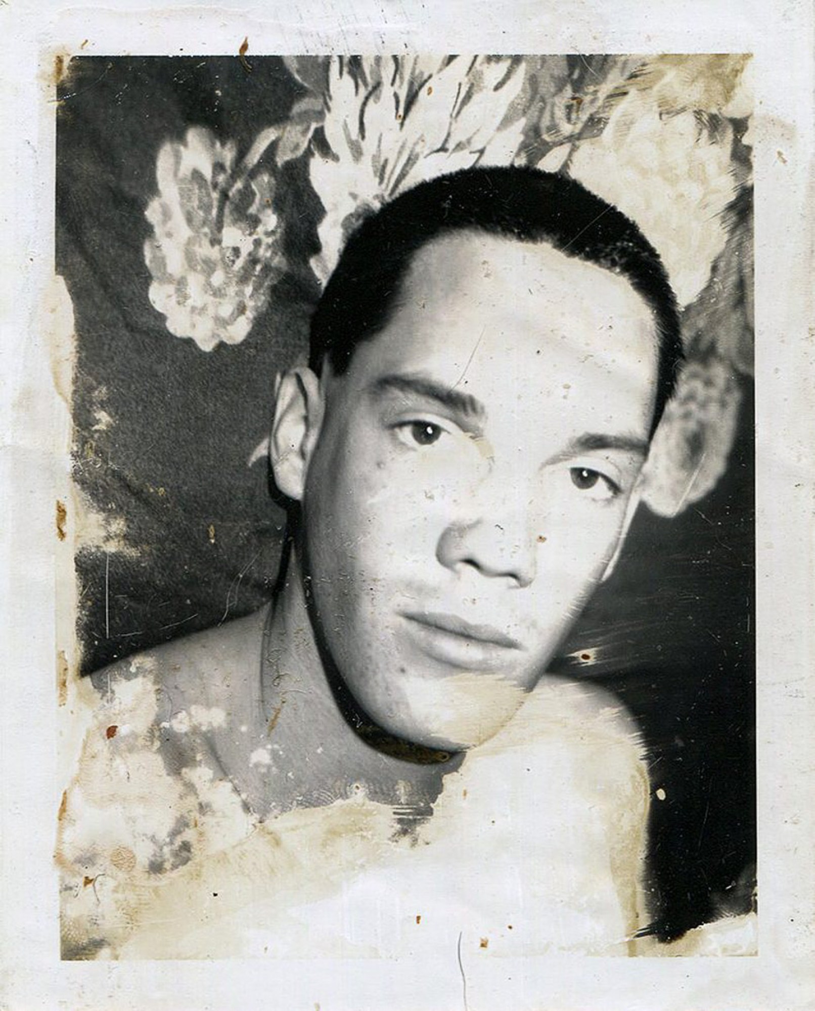 close up black and white polaroid of a man standing in front of floral fabric