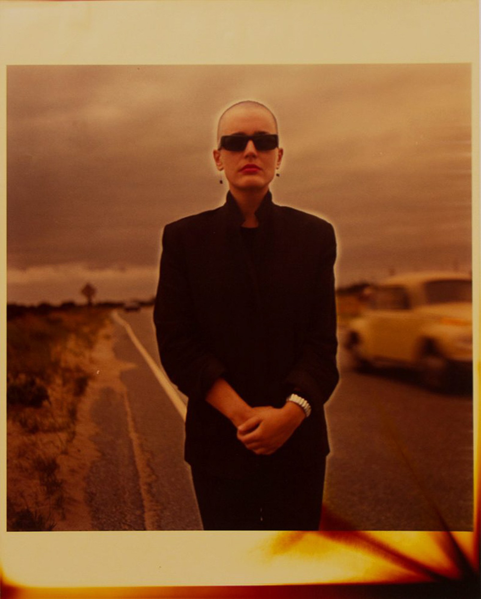 Pat Hearn standing on an empty road in a black suit and sunglasses