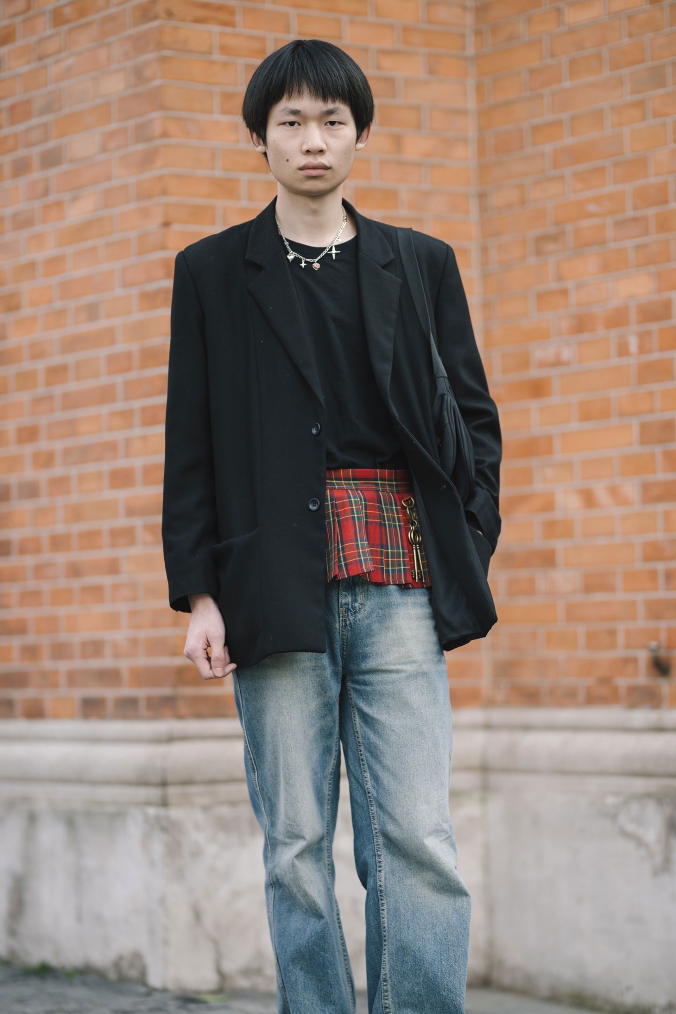 a man wearing jeans, a jacket and a tiny kilt poses neutrally for the camera