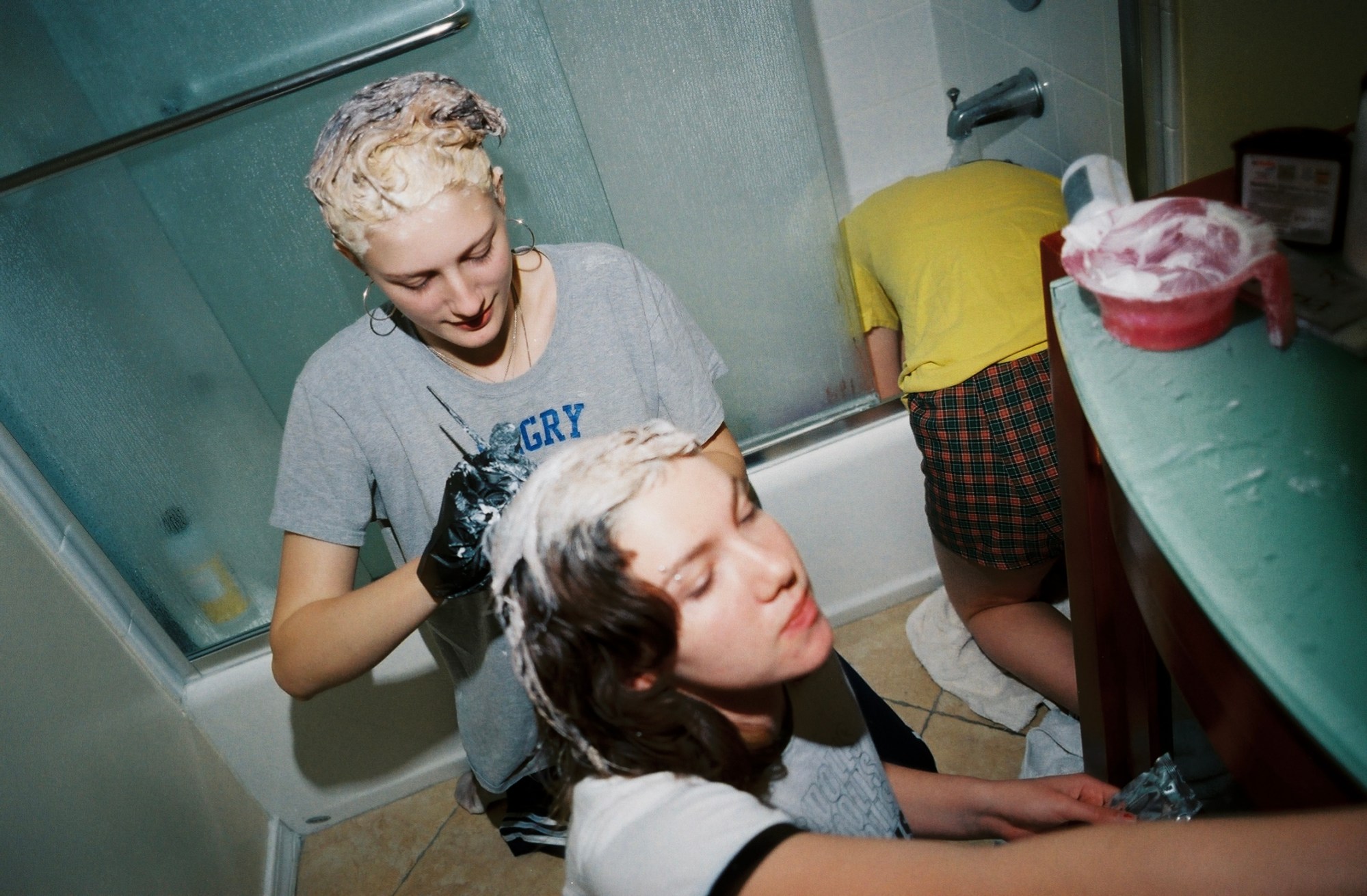 Two women dyeing their hair blonde on the floor of a bathroom