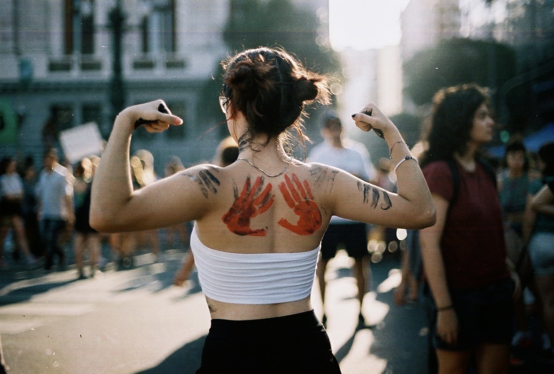 A woman poses with flexed biceps from behind, with red hands painted on her back