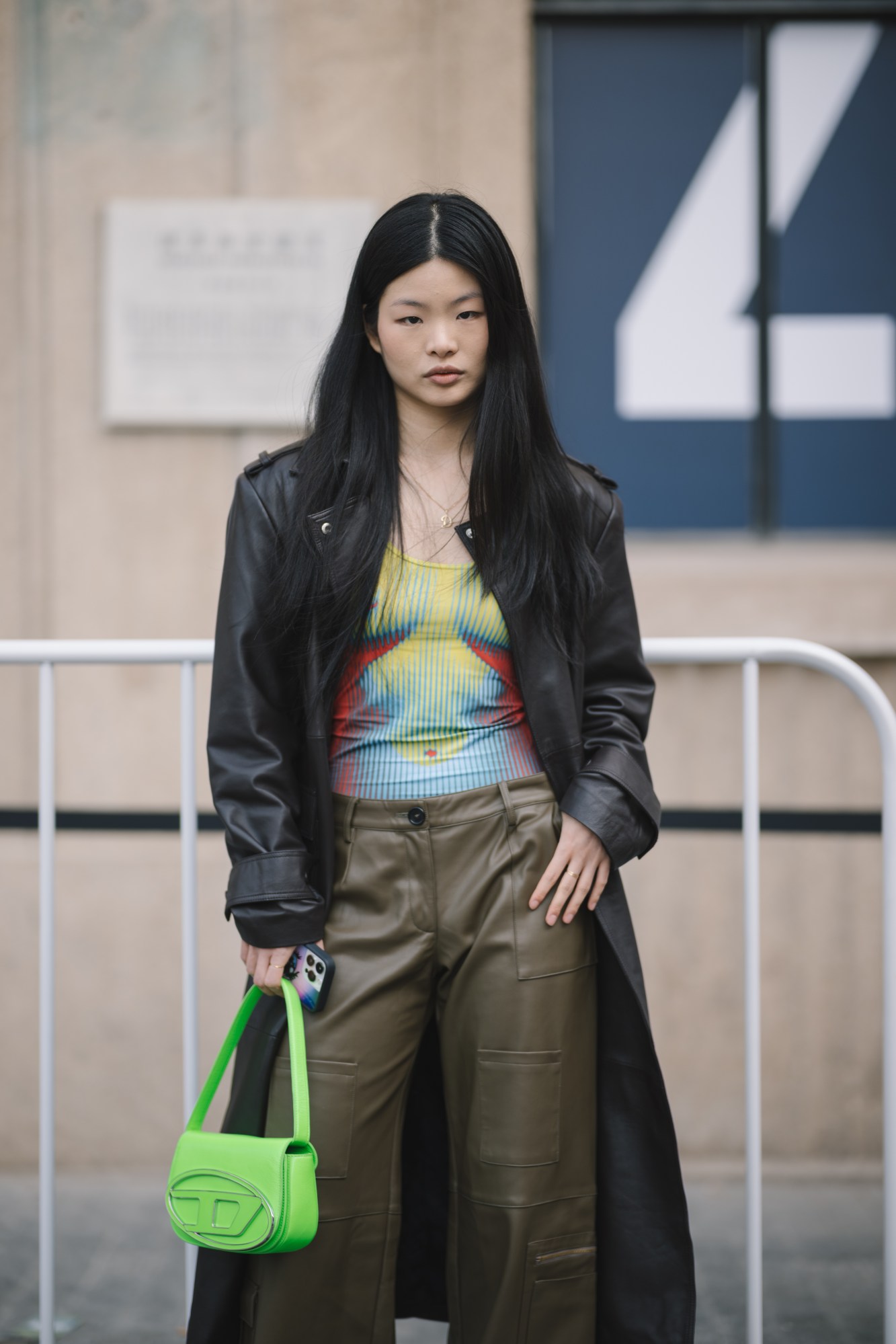 a woman wearing leather and a body-print vest top holds a bright green Diesel handbag