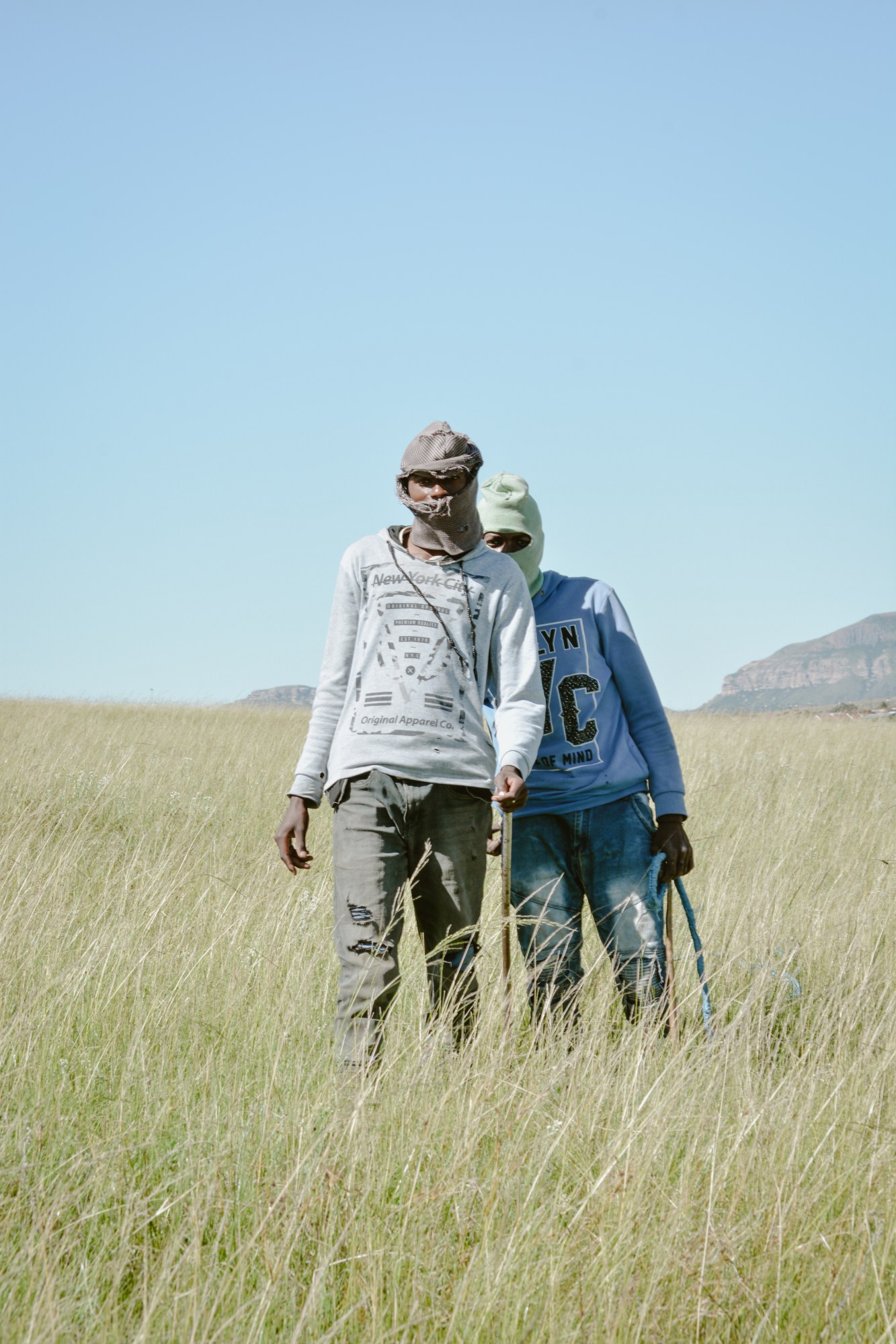 Two men in balaclavas stand in the middle of an empty green field