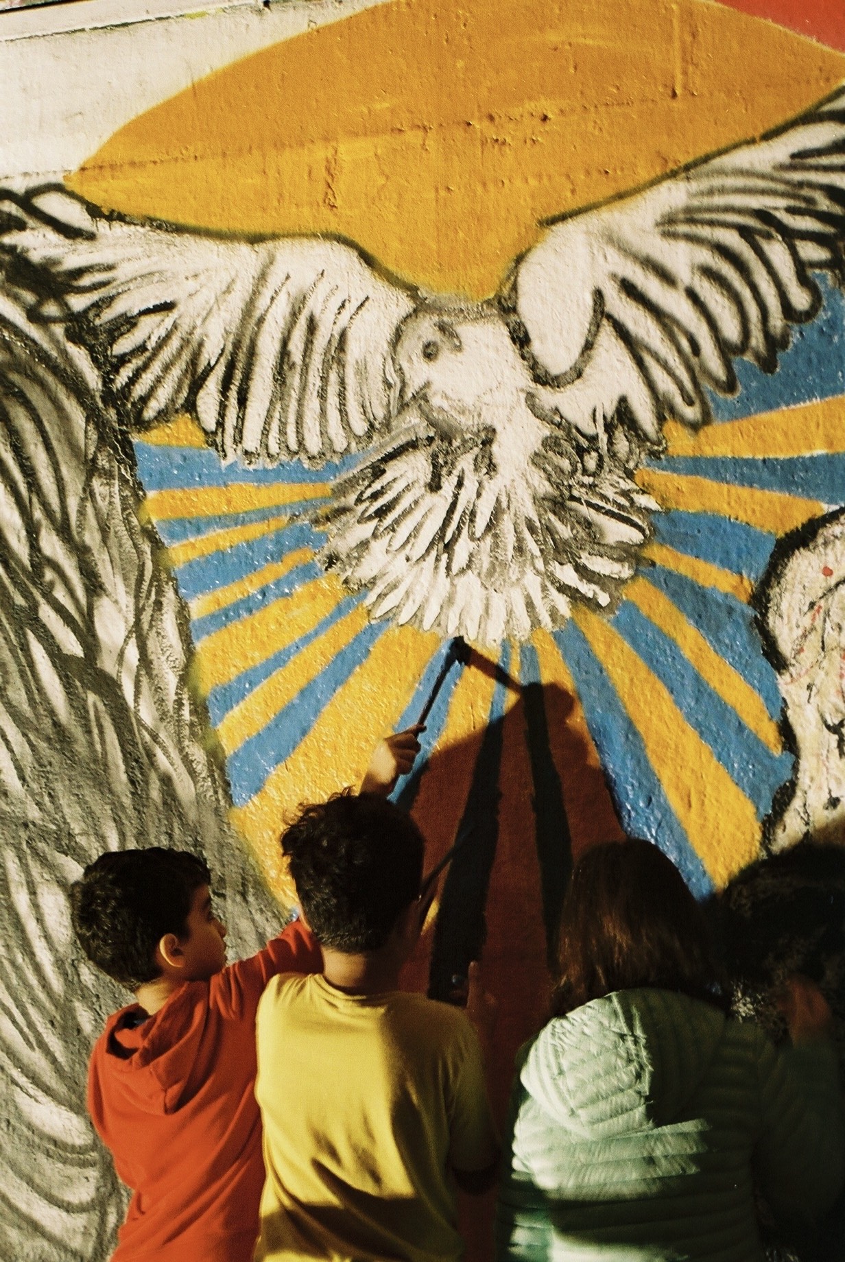 Children draw on a wall covered in a mural of a bird flying through blue and yellow light