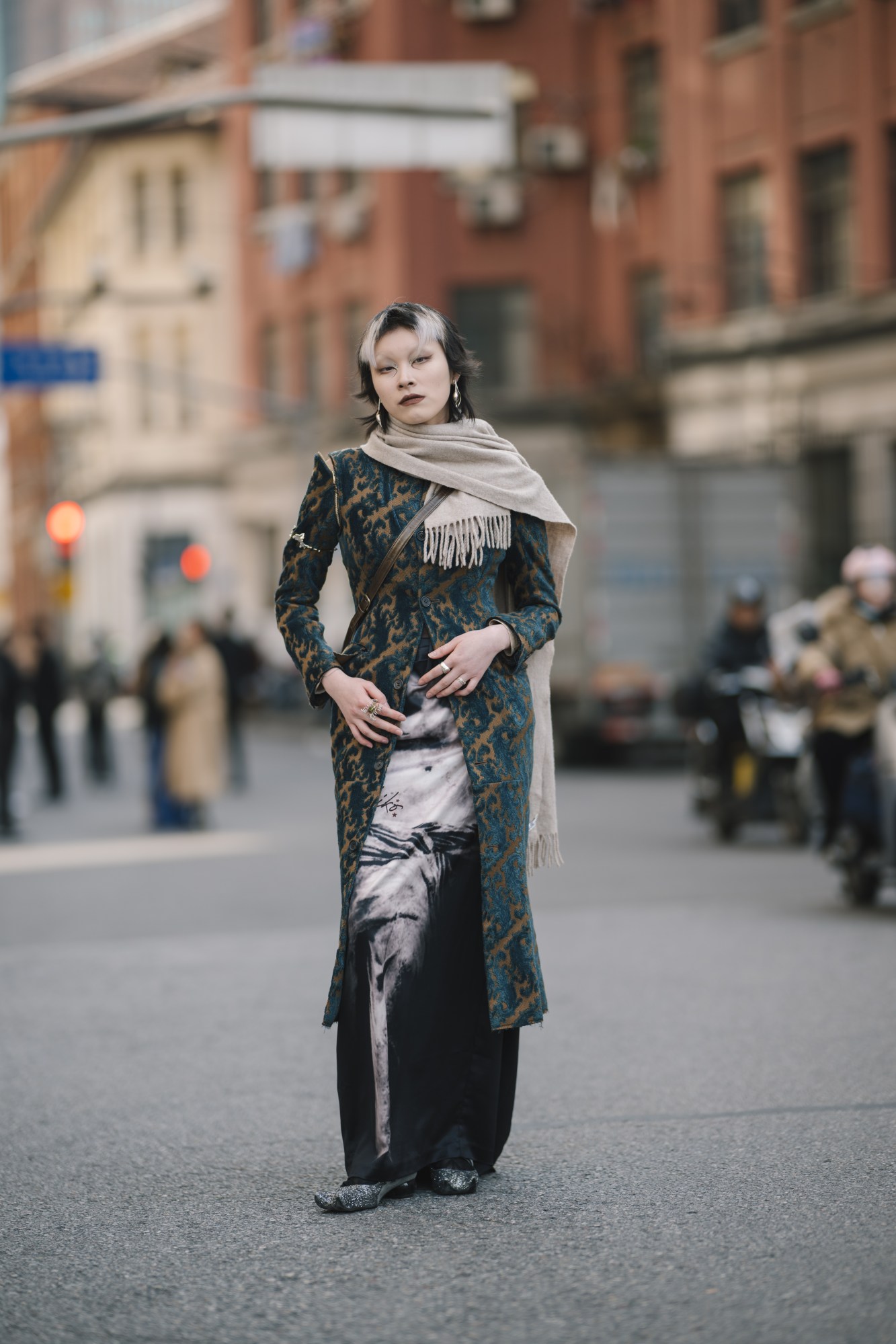 a person dressed for fashion week poses; the front of their hair is bleached white and their eye makeup is experimental