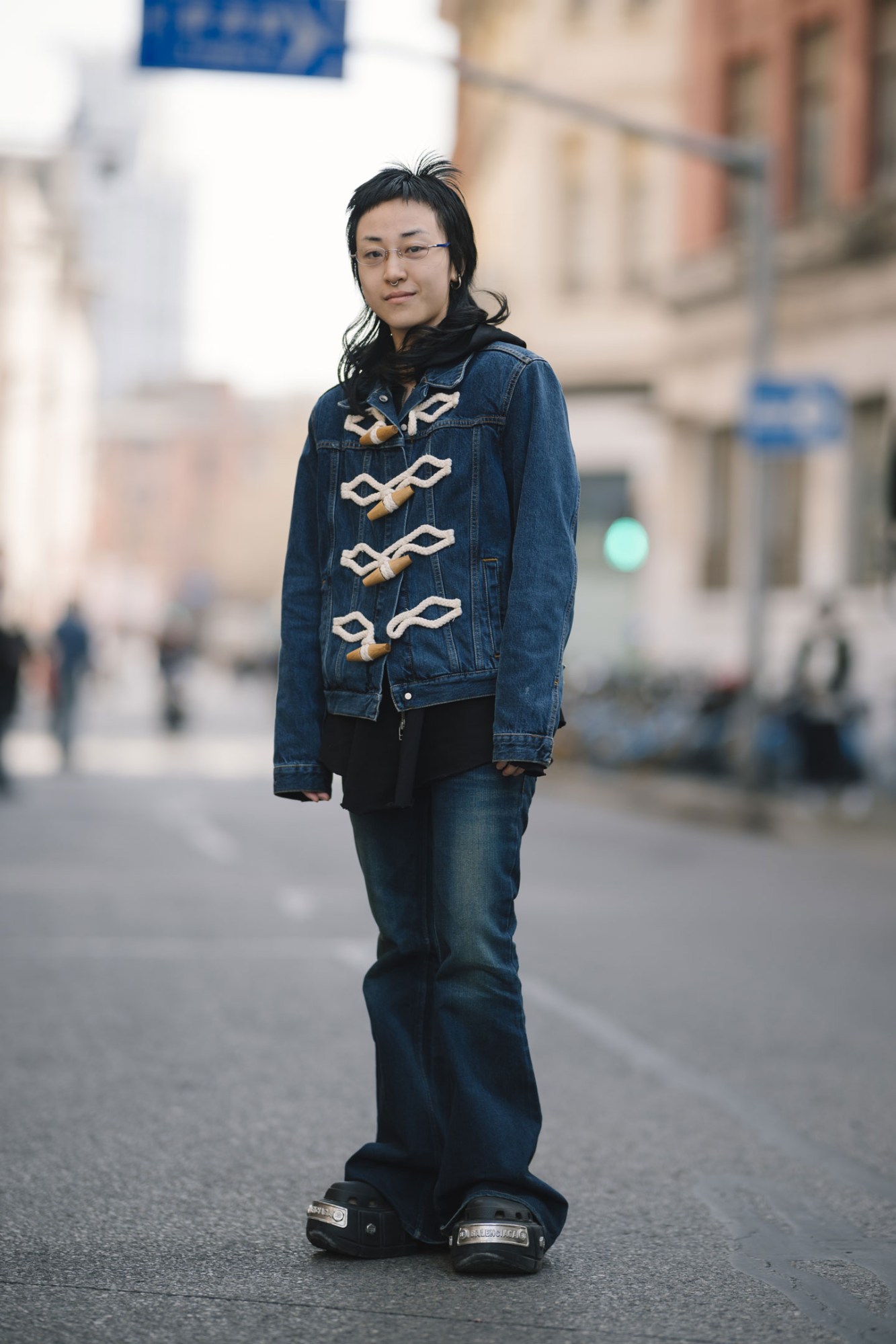 a person with a fashion mullet wears a denim jacket with oversized toggles