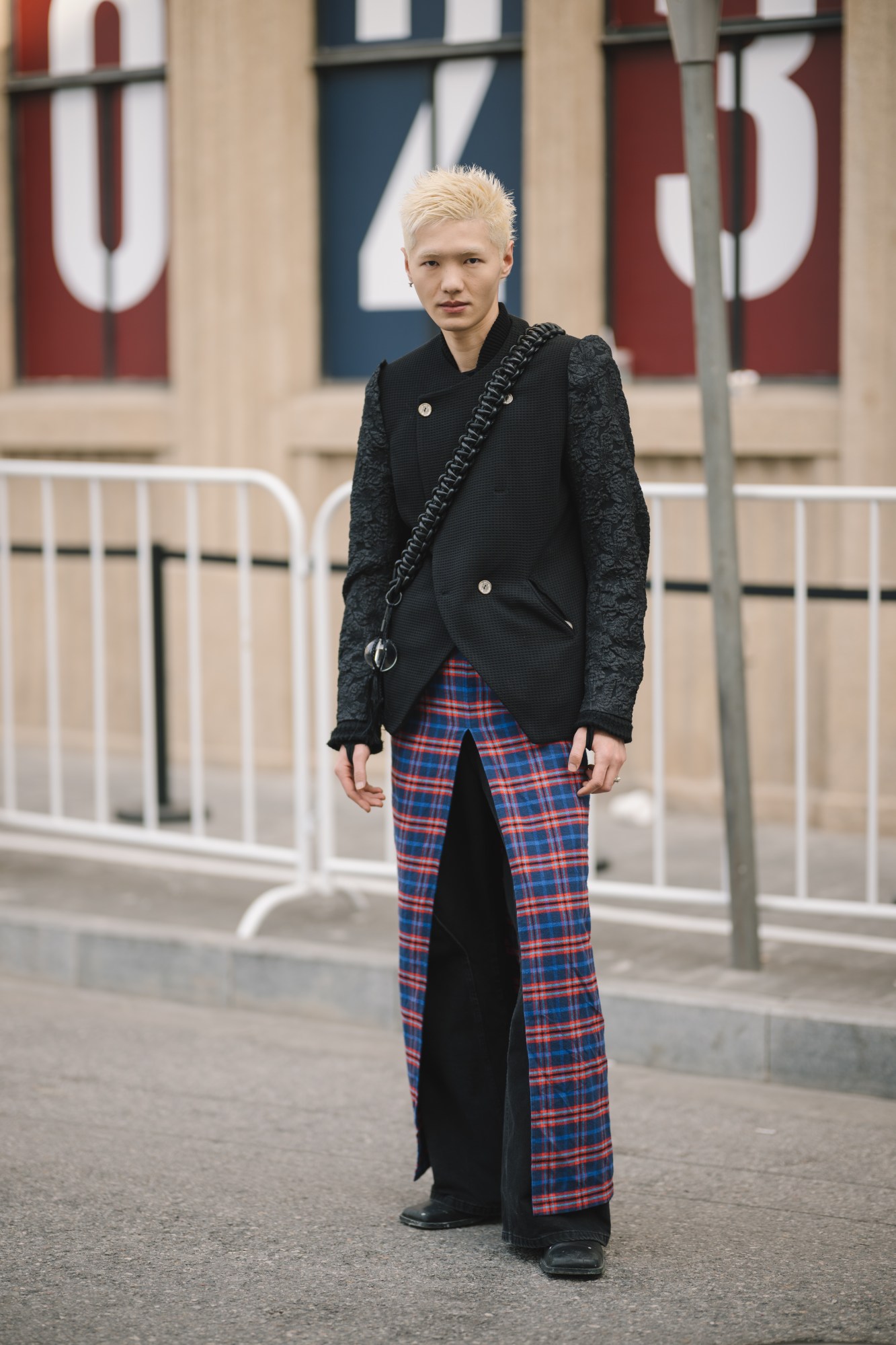 a model with bleached spiky hair wears a plaid skirt over black jeans