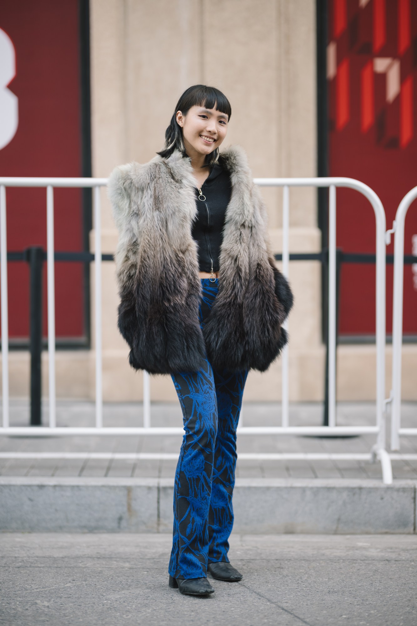 a girl in electric blue patterned trousers and a faux fur coat smiles to the camera