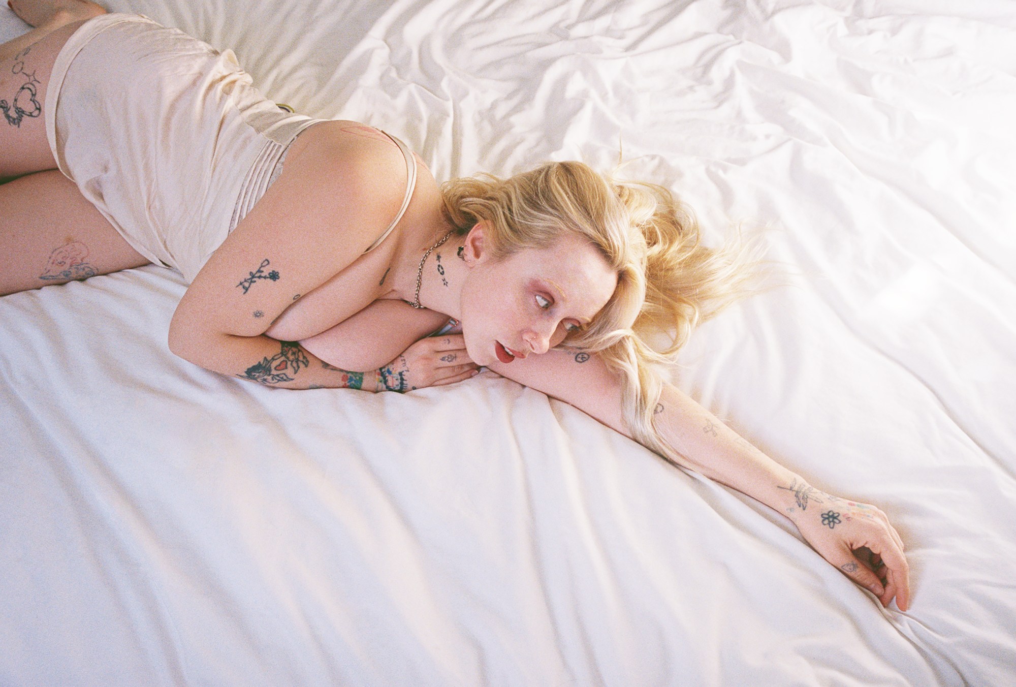 Harmony Tividad photographed by Morgan Maher lying across a white bed with her arms stretched out