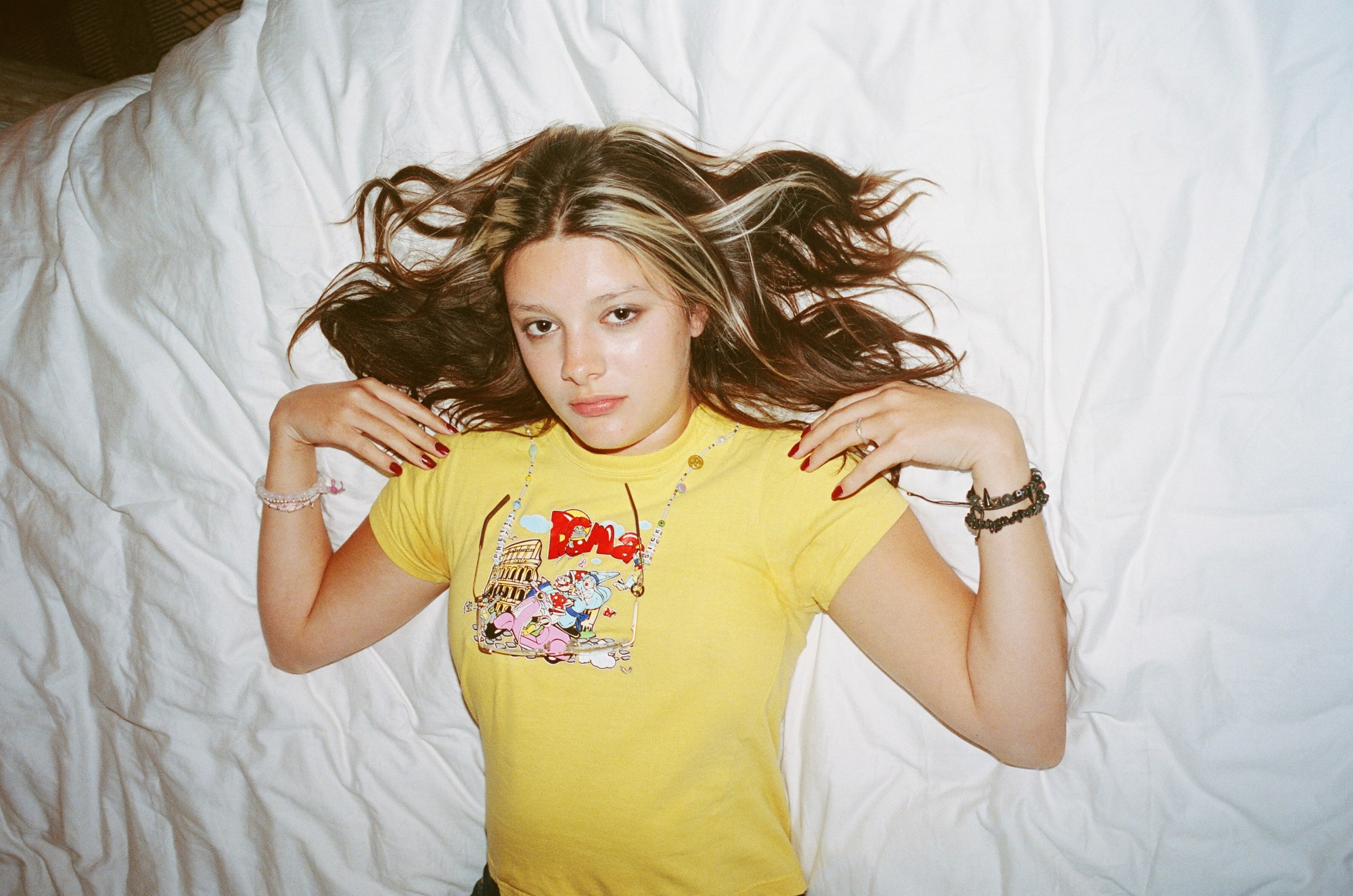 Sabrina Fuentes photographed by Morgan Maher in a yellow tshirt with her hair spread across a white bed