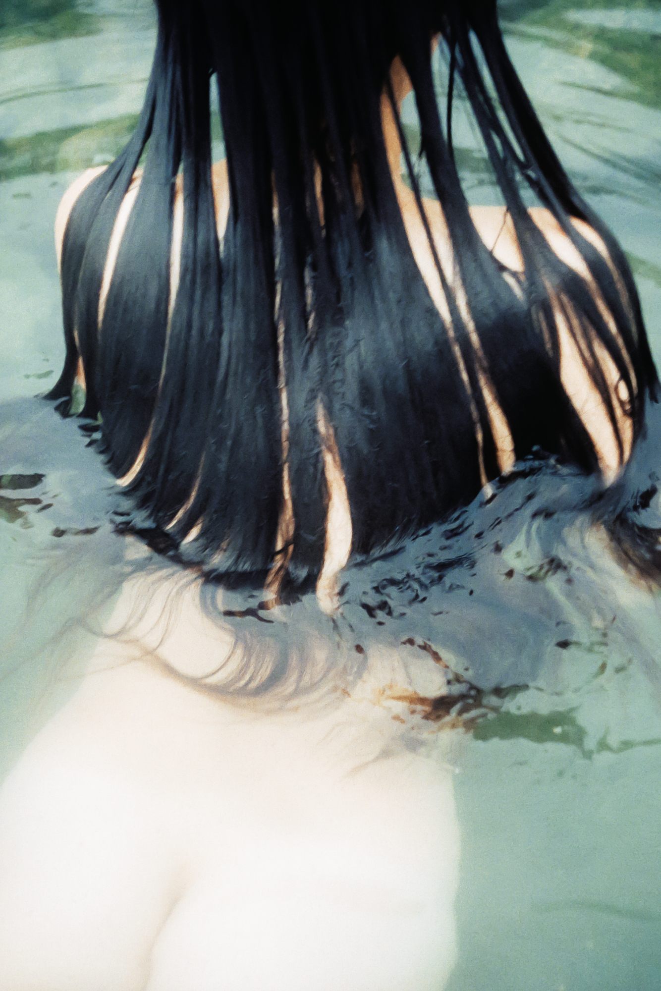 Close up of a woman swimming naked in a Japanese wild hot spring, shot from behind with her hair splayed behind her