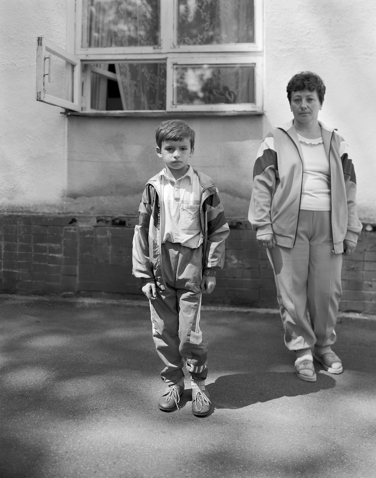 Black-and-white image of a young boy with his mum standing in front of an open window