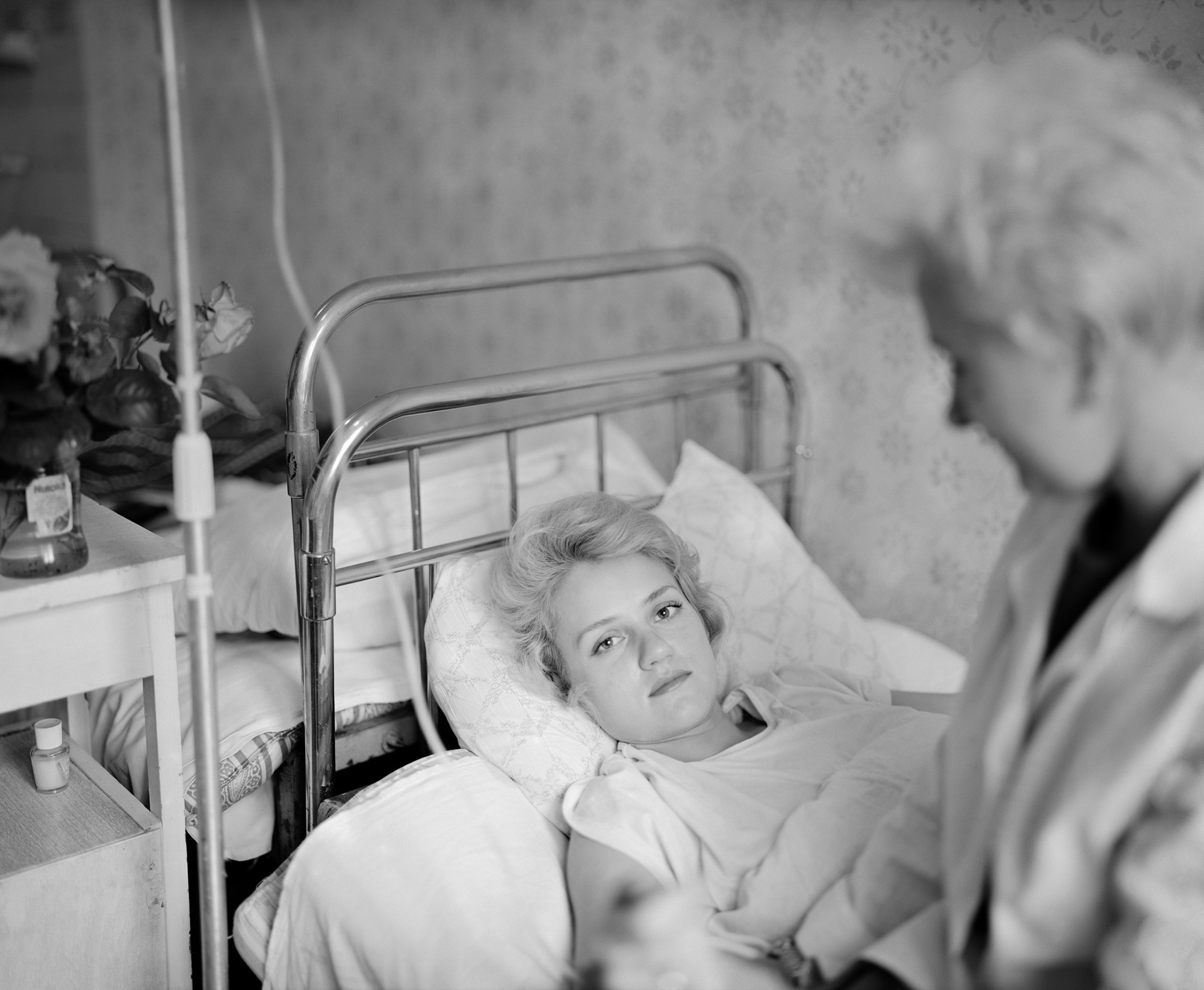 Black-and-white image of a blonde woman lying in a hospital bed