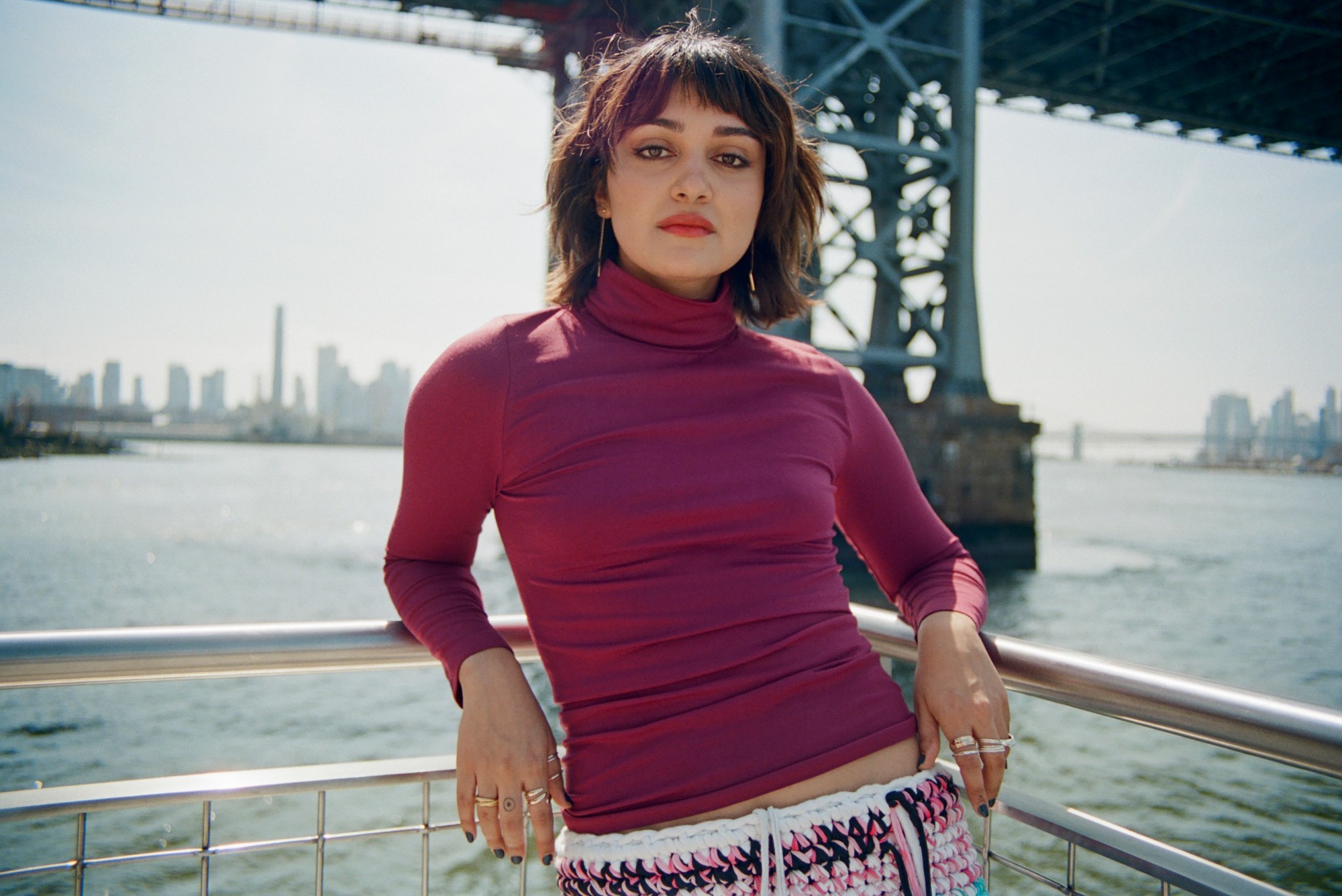 ariela in a magenta roll neck and low-waist woven skirt posing in front of a river