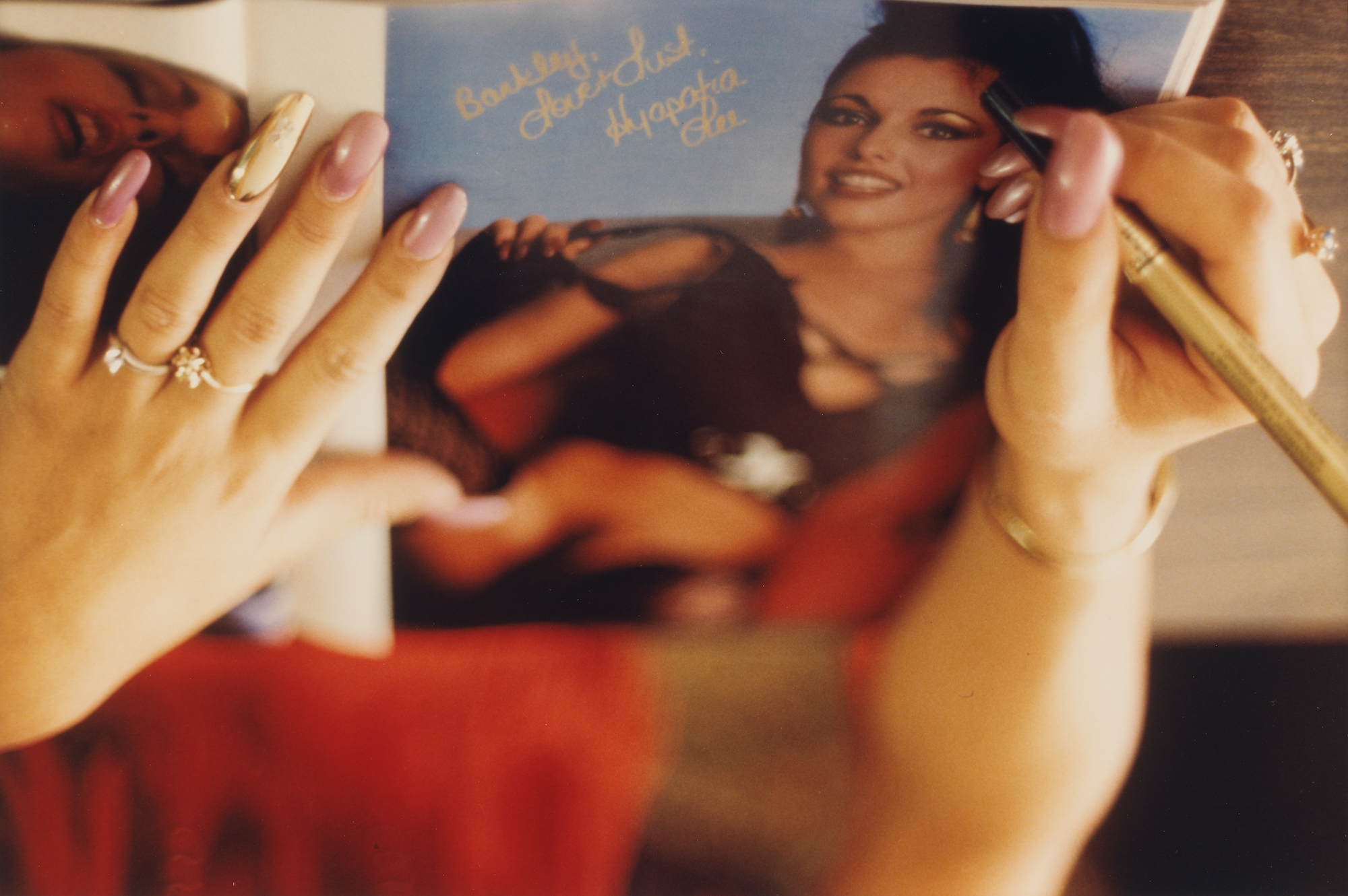 a woman with long pink and gold nails signing an autograph