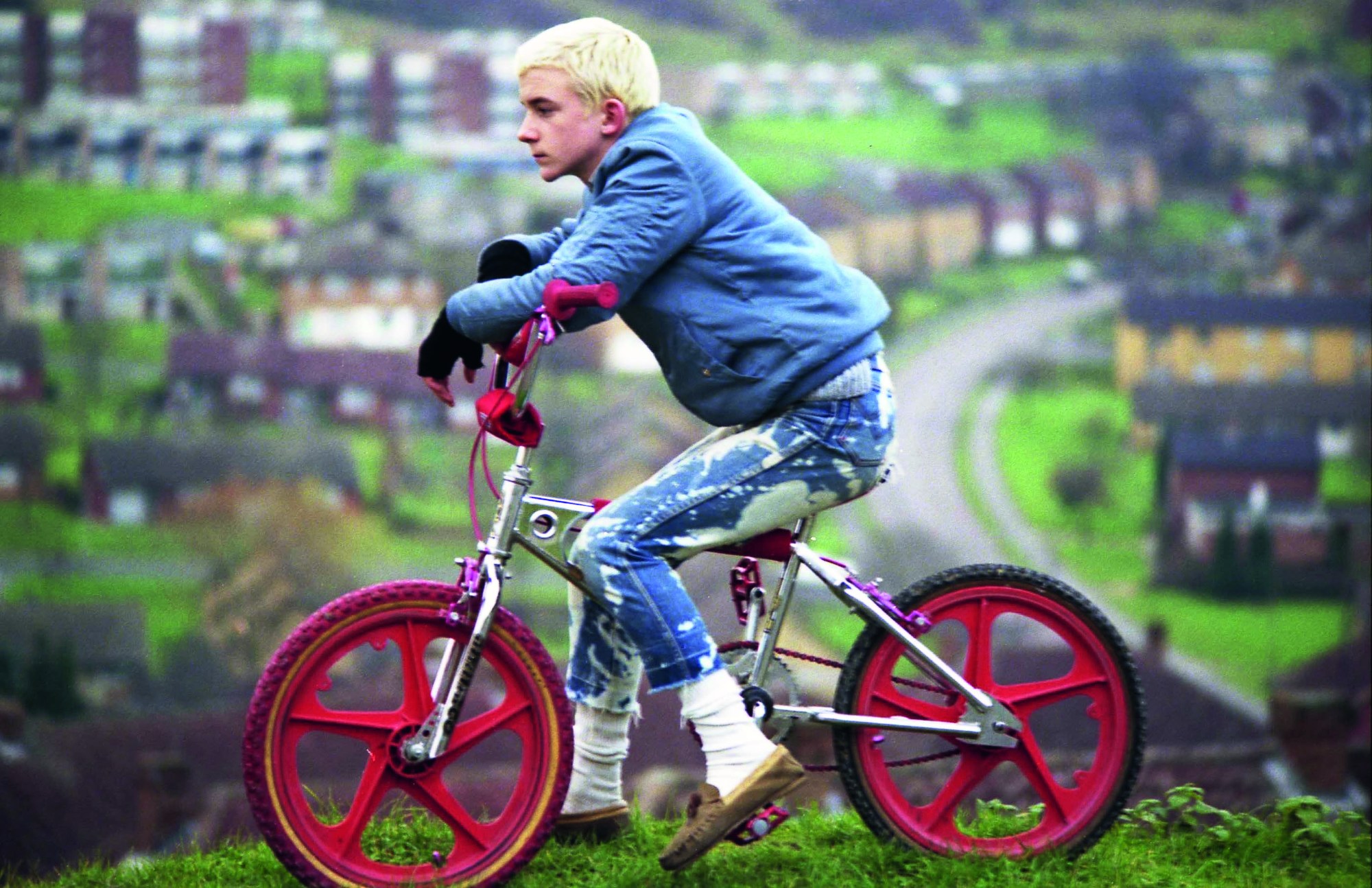 a young leach blonde boy sits on a bmx bike overlooking a suburban city scene