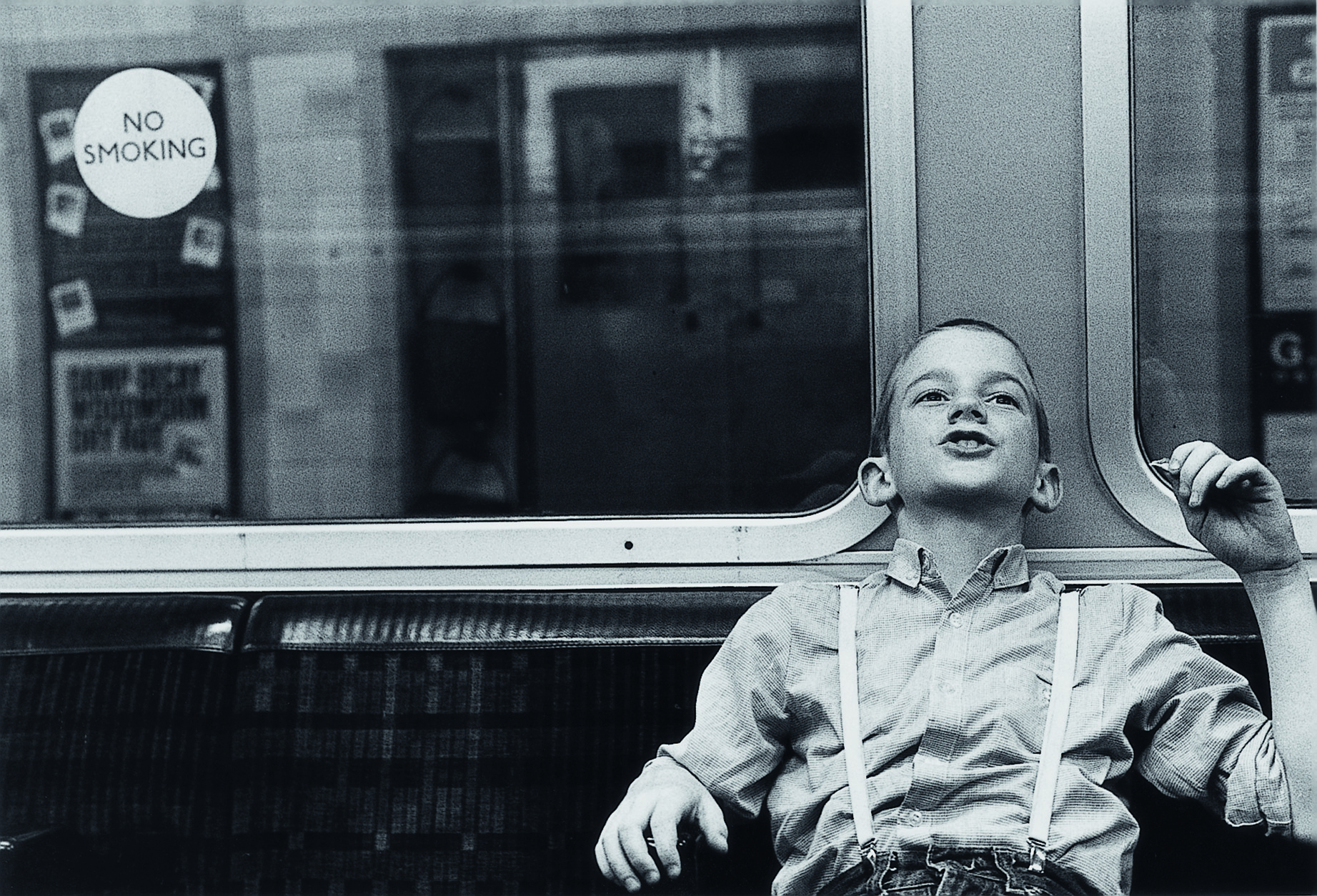 a young boy wearing suspenders sits leaning back on a bus