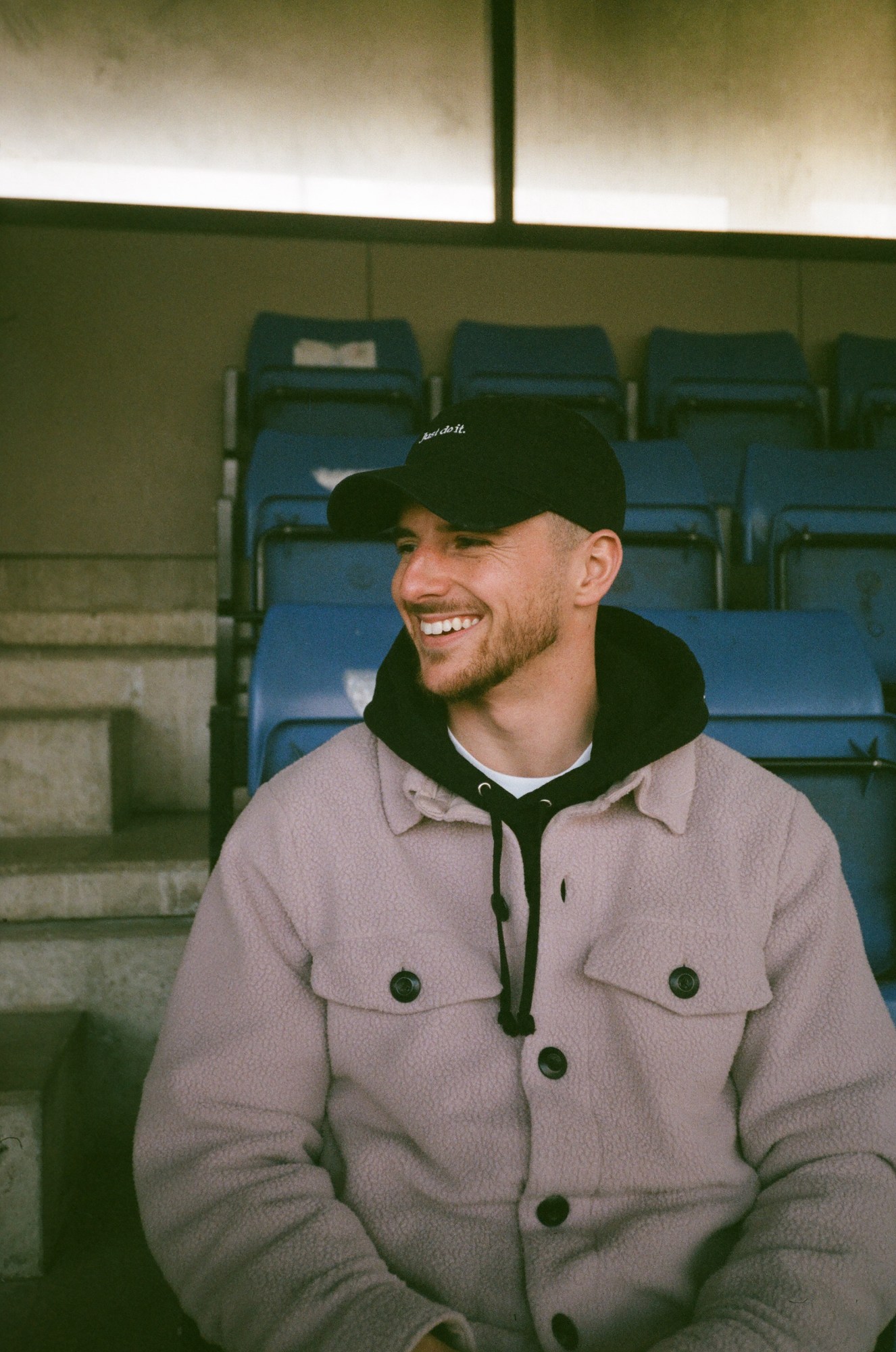 mason mount wearing black nike cap looking off camera as he smiles. he's wearing a fleece.