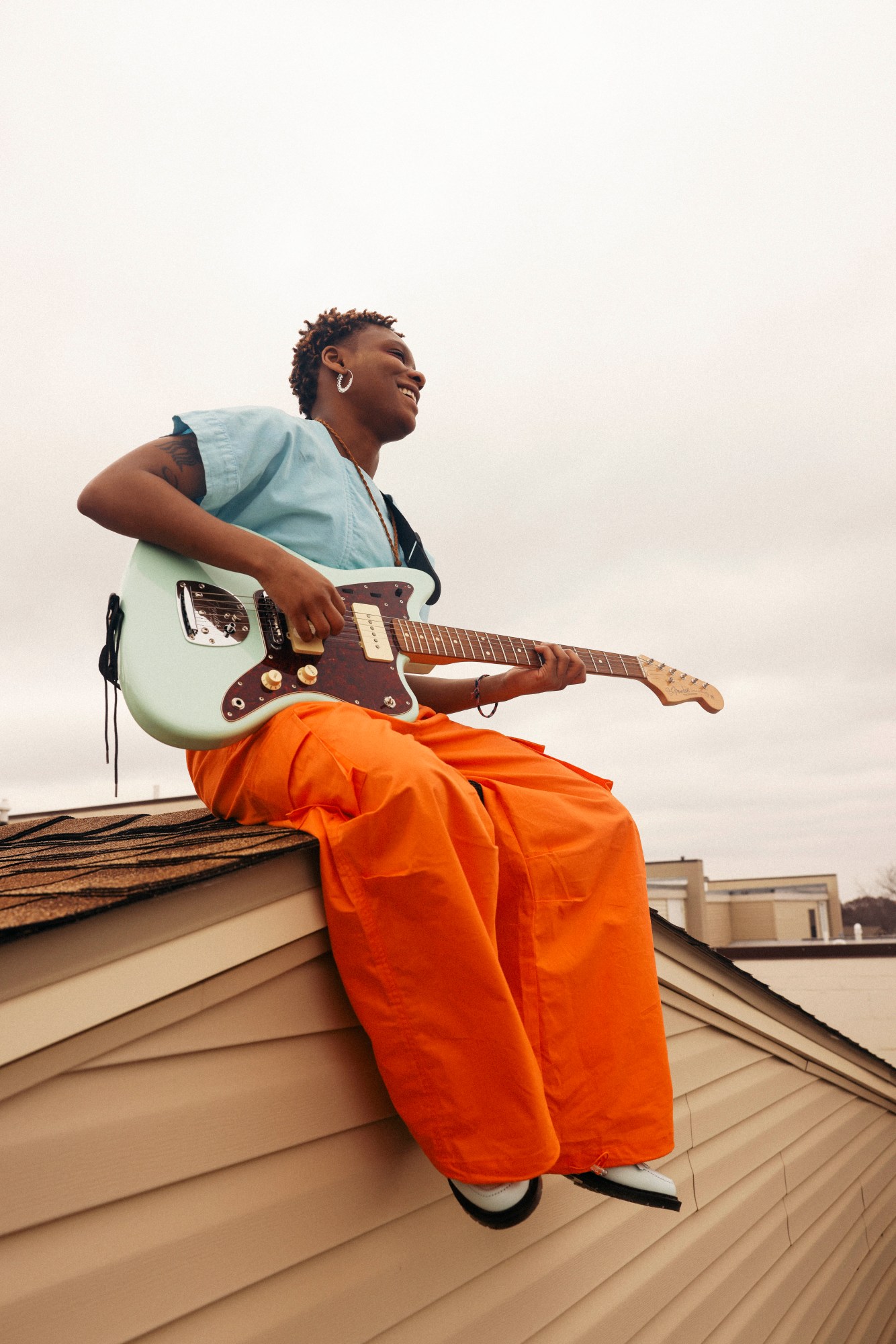 dreamer poses on a rooftop holding their guitar