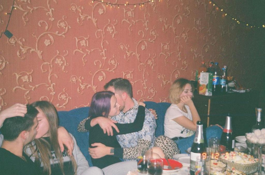 two couples making out on a couch and one person sitting solo in front of red wallpaper