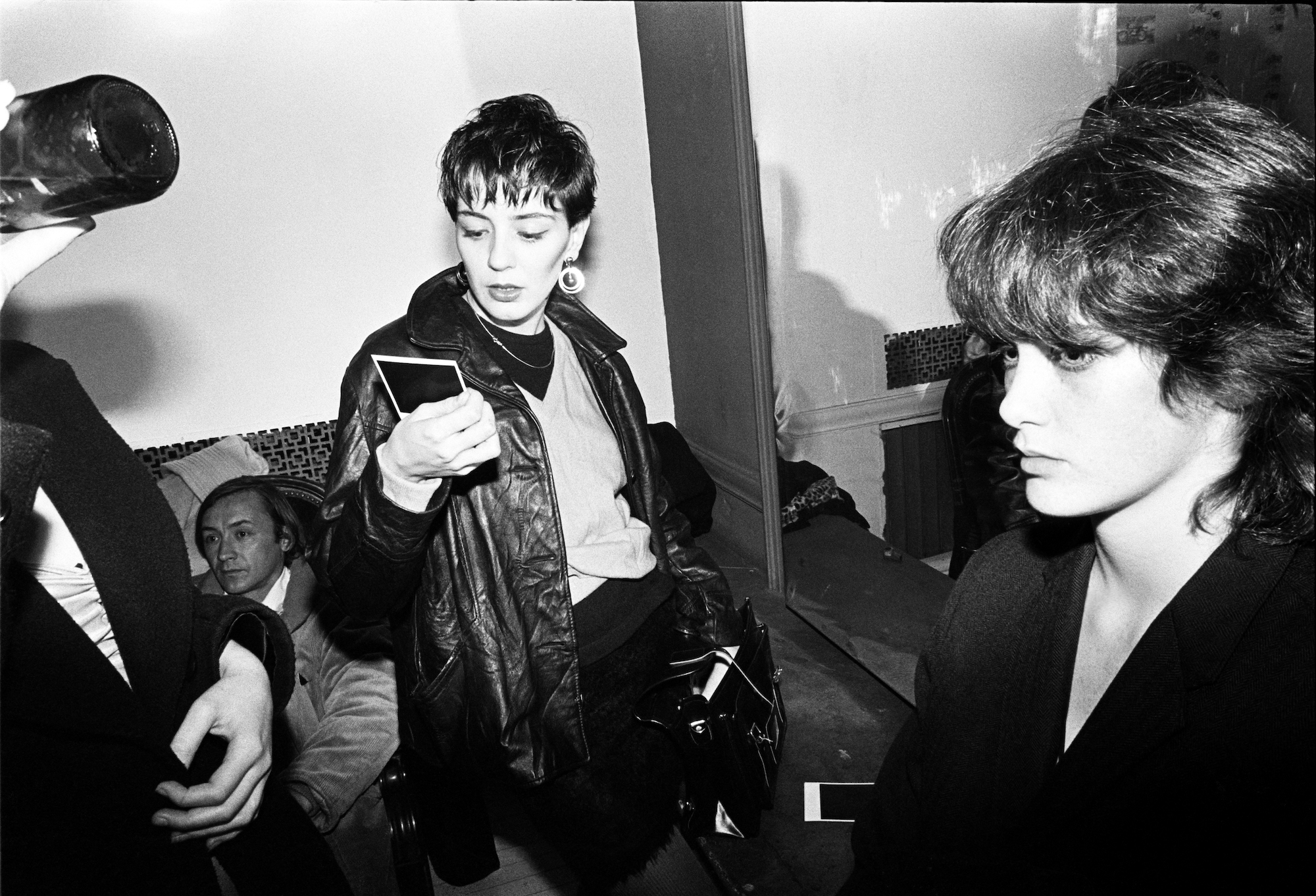 a woman in a black leather jacket looking at a polaroid at maripol squat theater