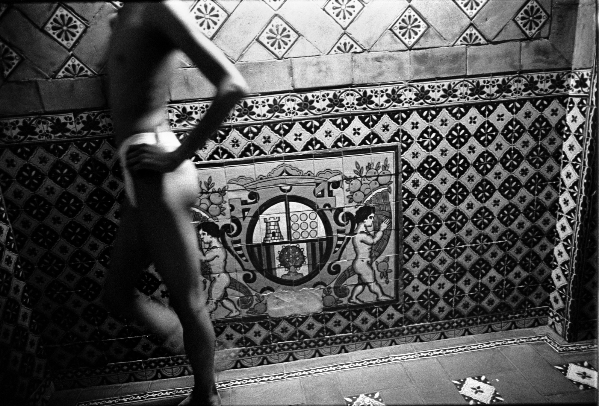 Black-and-white photograph by Joseph Rodriguez in Mexico City in the 90s of a sex worker in underwear standing by a tiled wall.