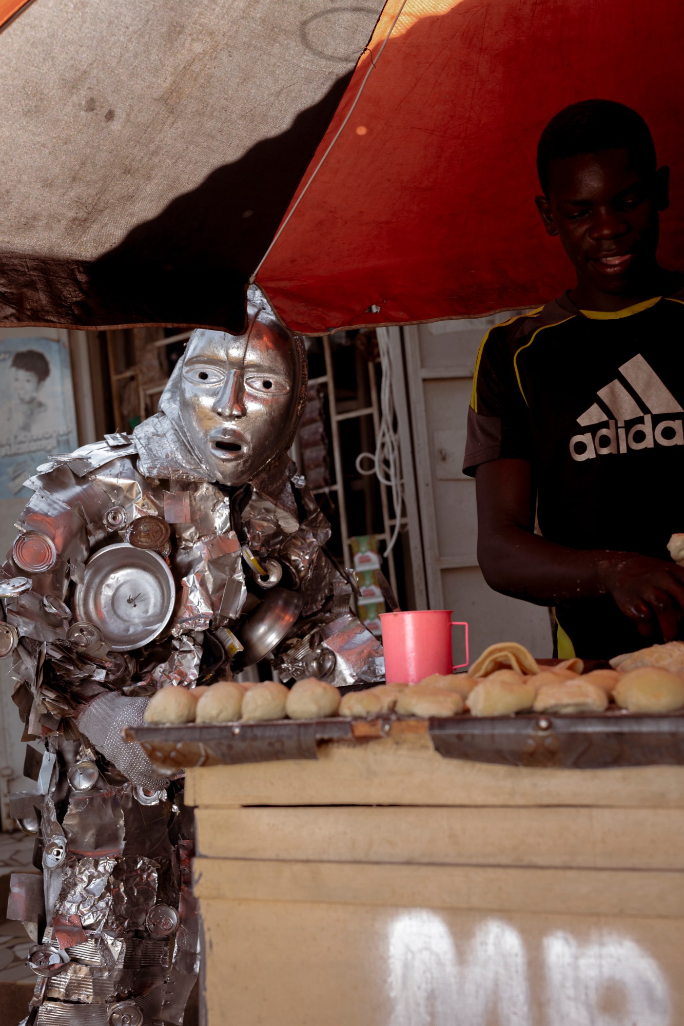 a man wearing a tin can costume at a food stand in uganda