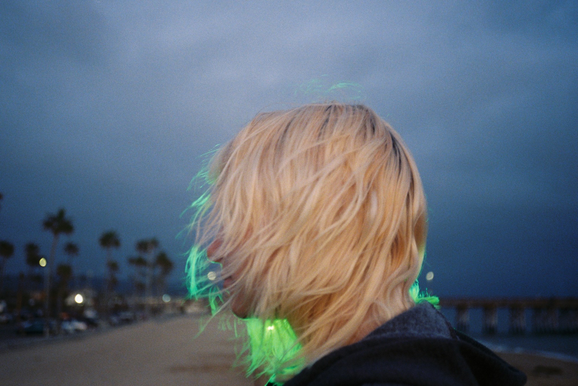 a blonde kid backlit by green neon light on the beach in california