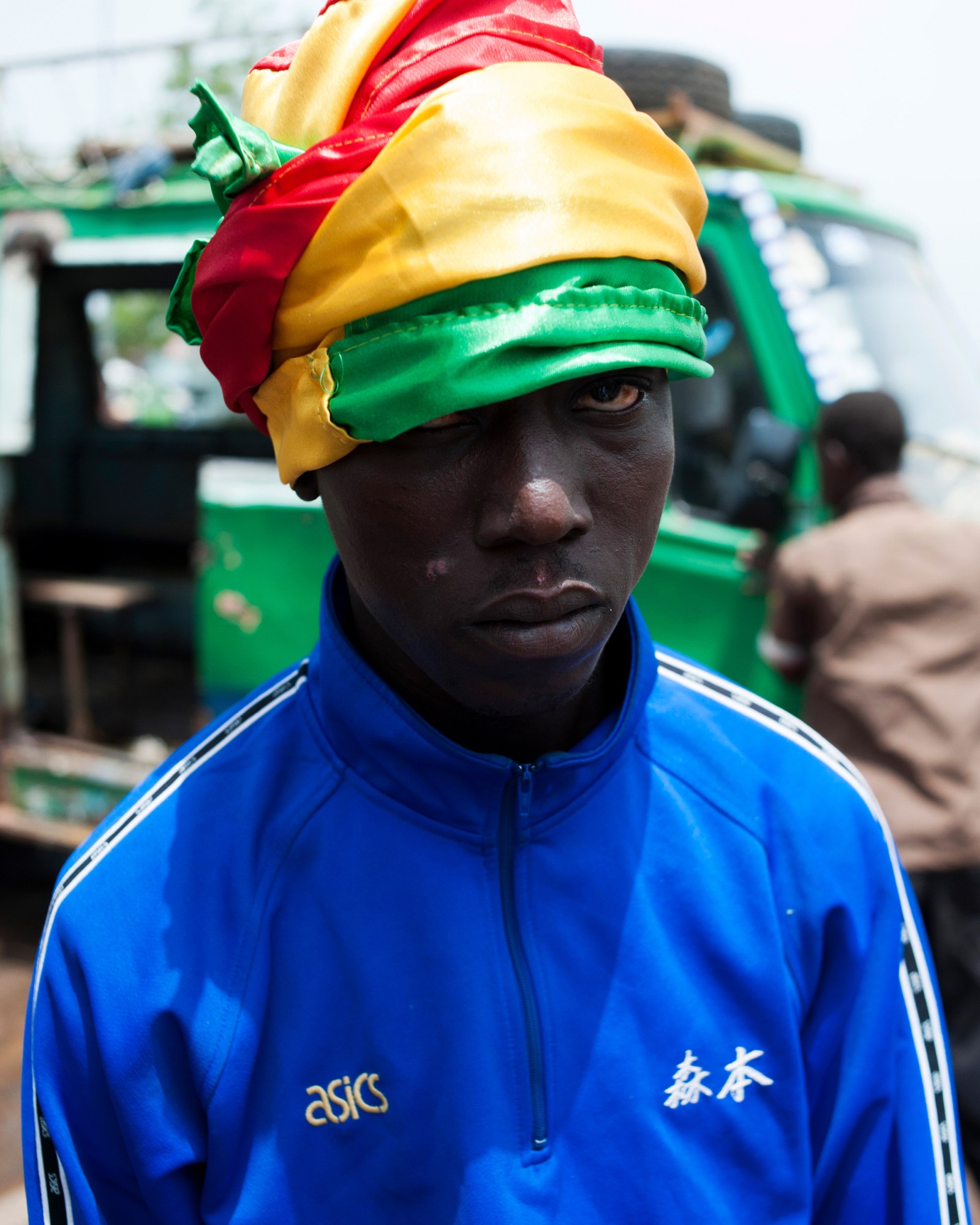 a young man in a blue pullover wearing a green, yellow, and red scarf on his head