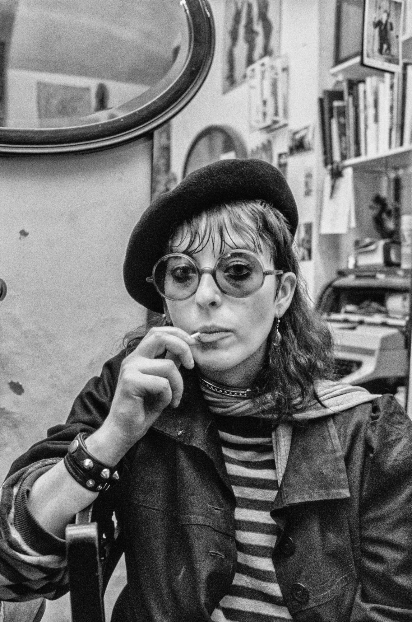 black and white picture of a young woman wearing round glasses with a lollipop in her mouth