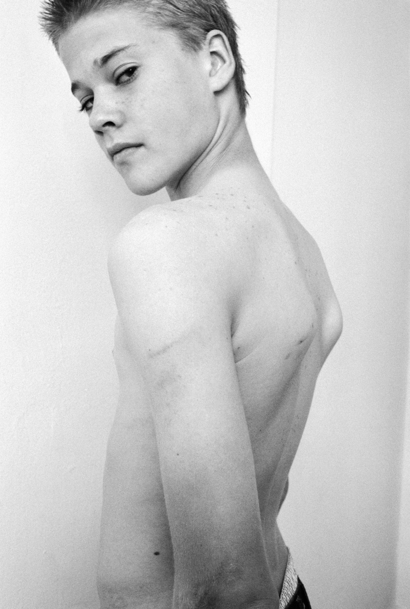 a young shirtless boy facing a white wall