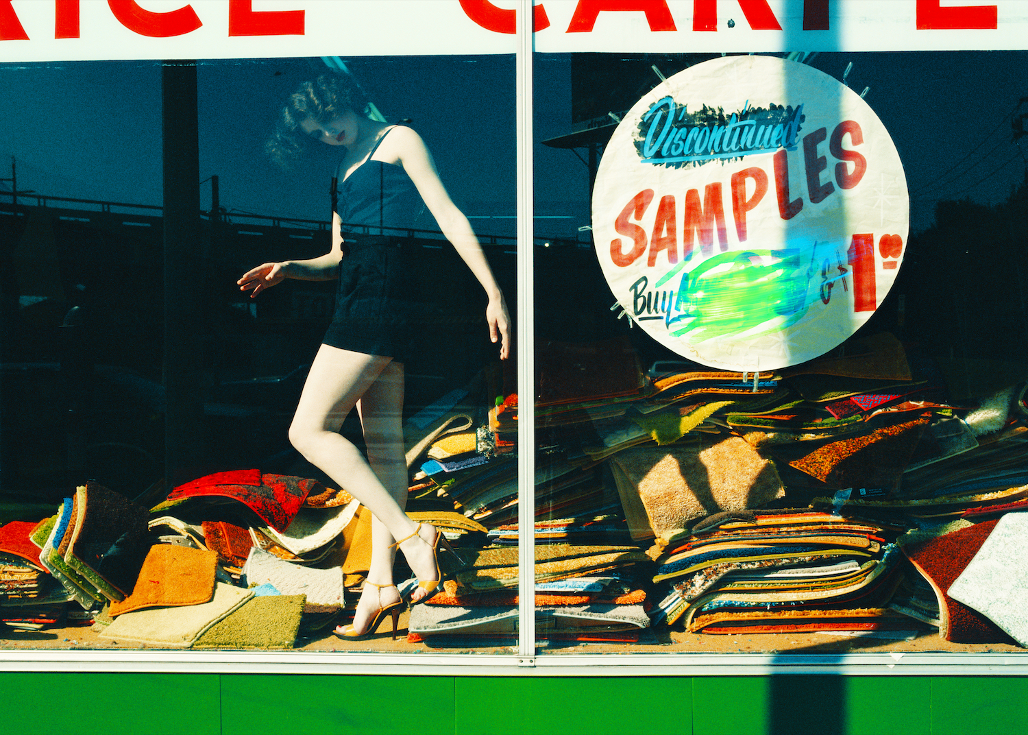 A woman in a black dress poses in a sample store window as though she's a mannequin