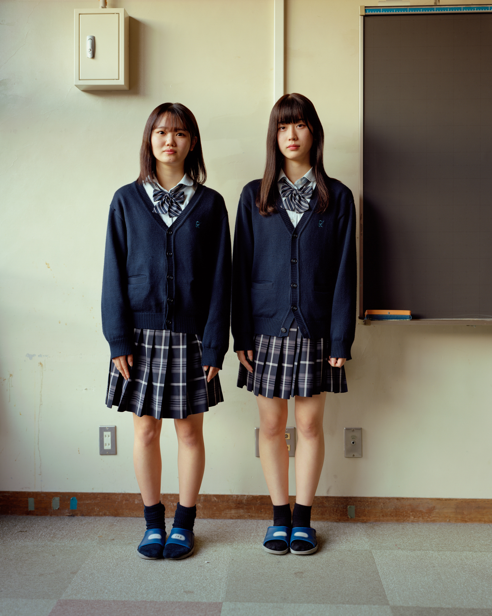 two japanese school girls stand side by side at a blackboard in a classroom