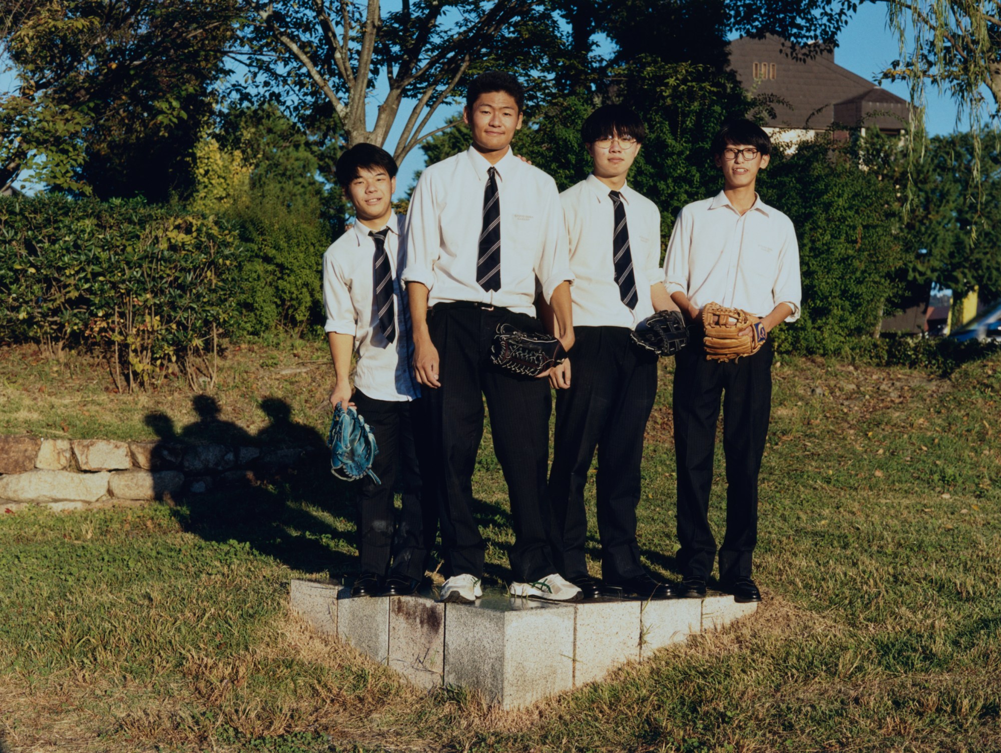 Four teenage boys with baseball mitts pose on a grass verge in Japan