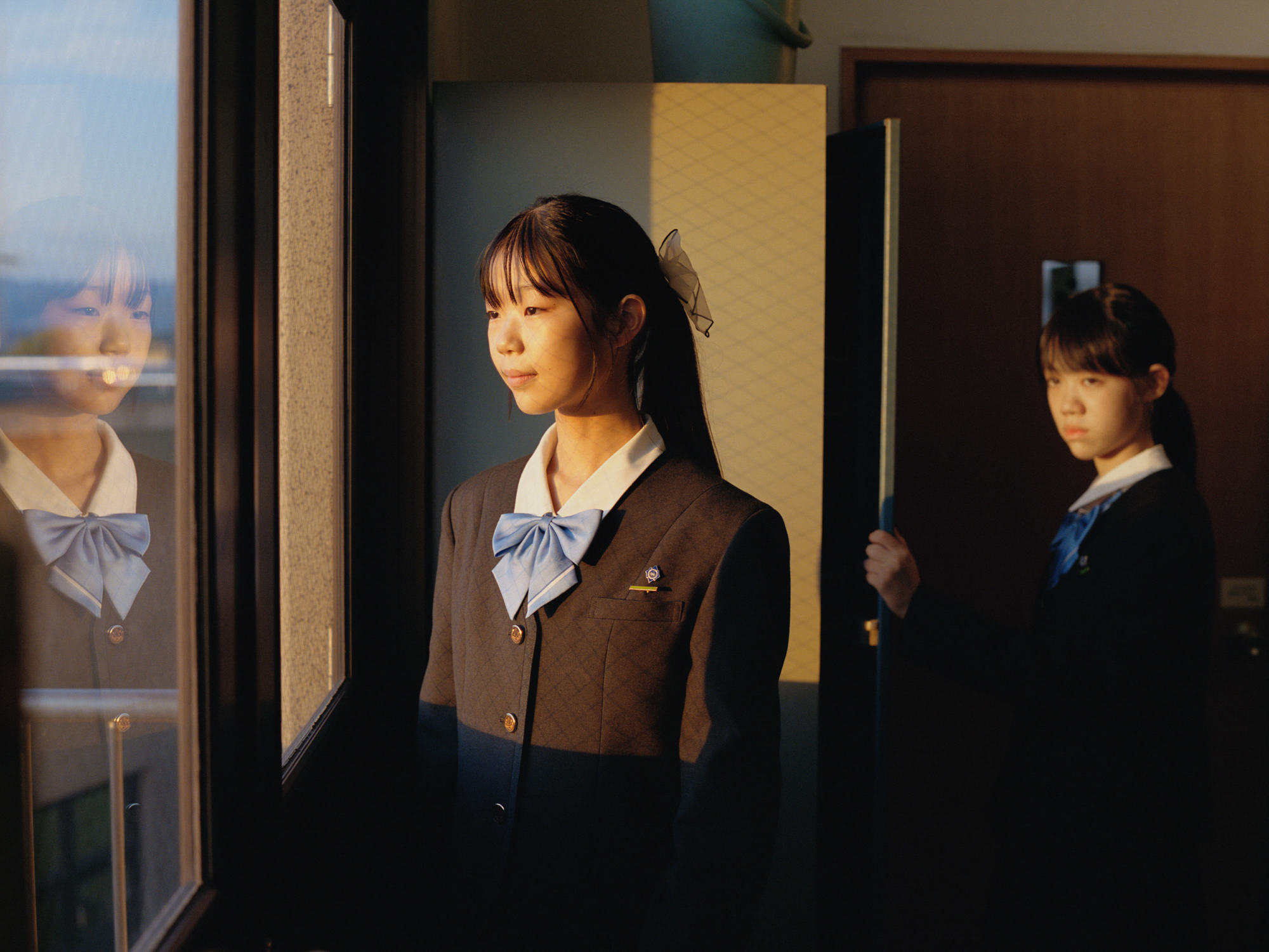 Two Japanese school girls looking in profile out of a window at sunset