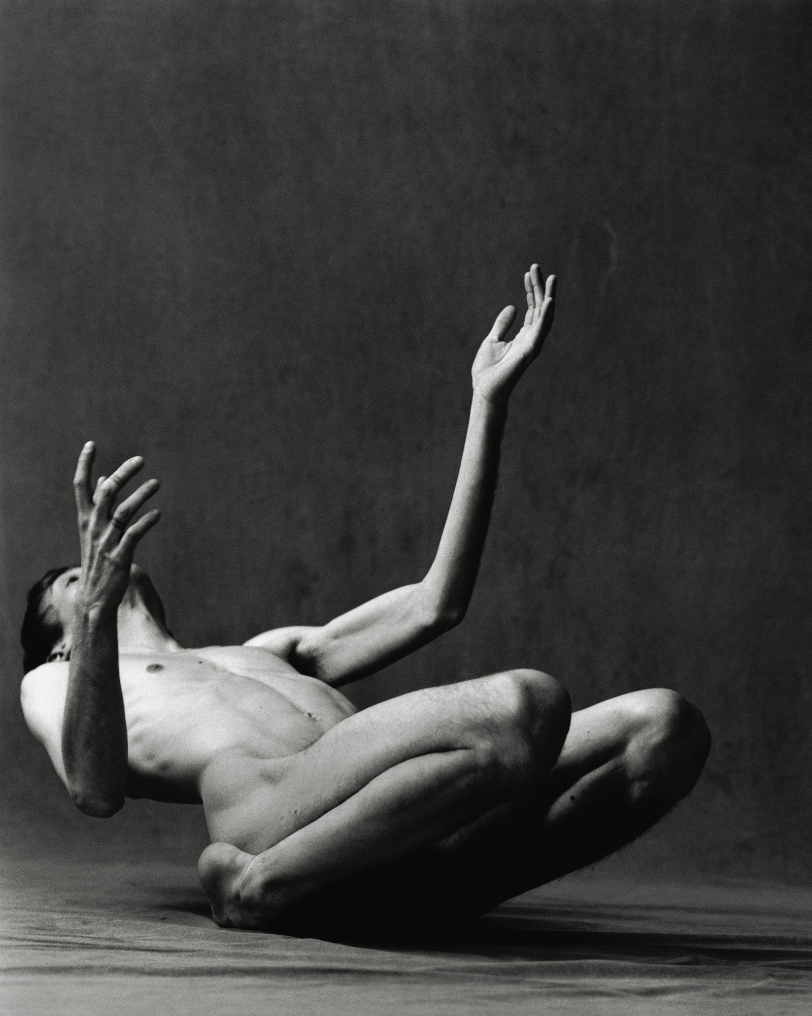 a white man falls backward on his knees, head stretched back with his arms up in a photo studio