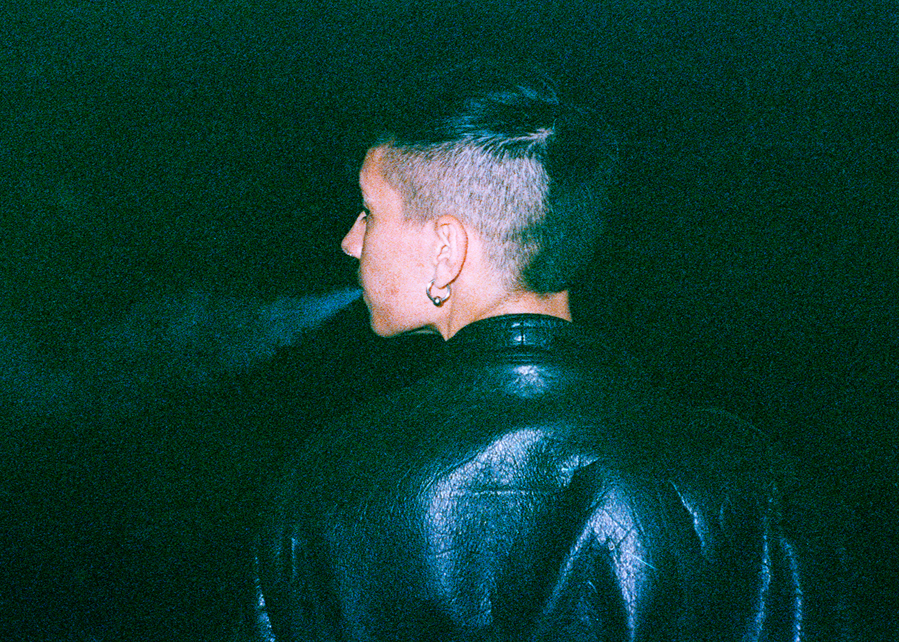 a young man wearing a leather jacket blowing cigarette smoke