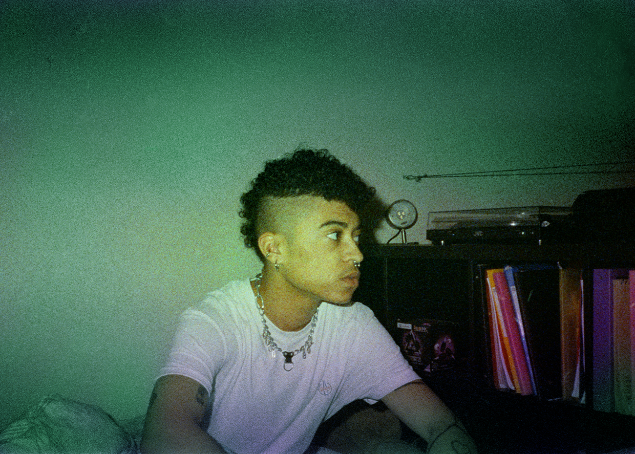 a young man with silver jewelry sitting near a bookshelf