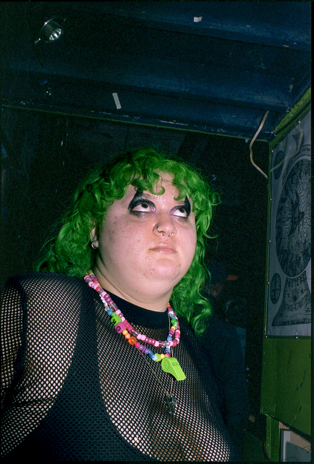 a raver with green hair and colorful kandi necklaces wearing a black mesh top at the rave