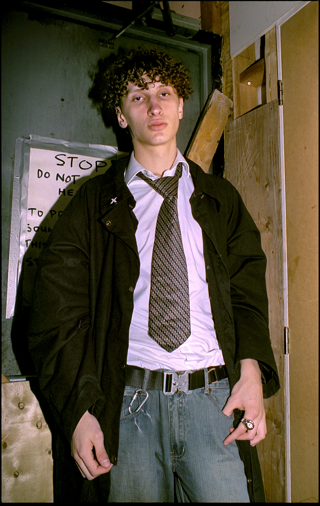 a young raver with a tie and seatbelt belt posing in the doorway at a rave in toronto