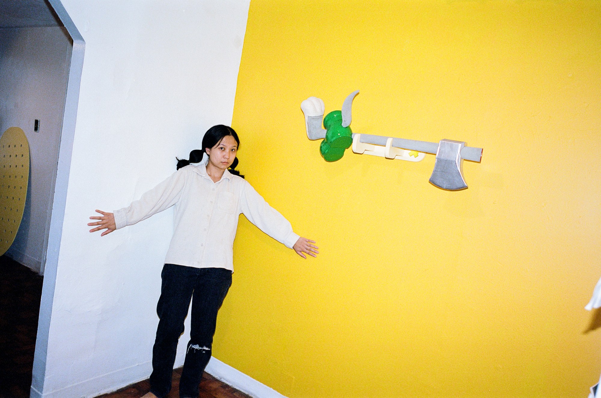 april zhu standing in front of a yellow wall at her gallery