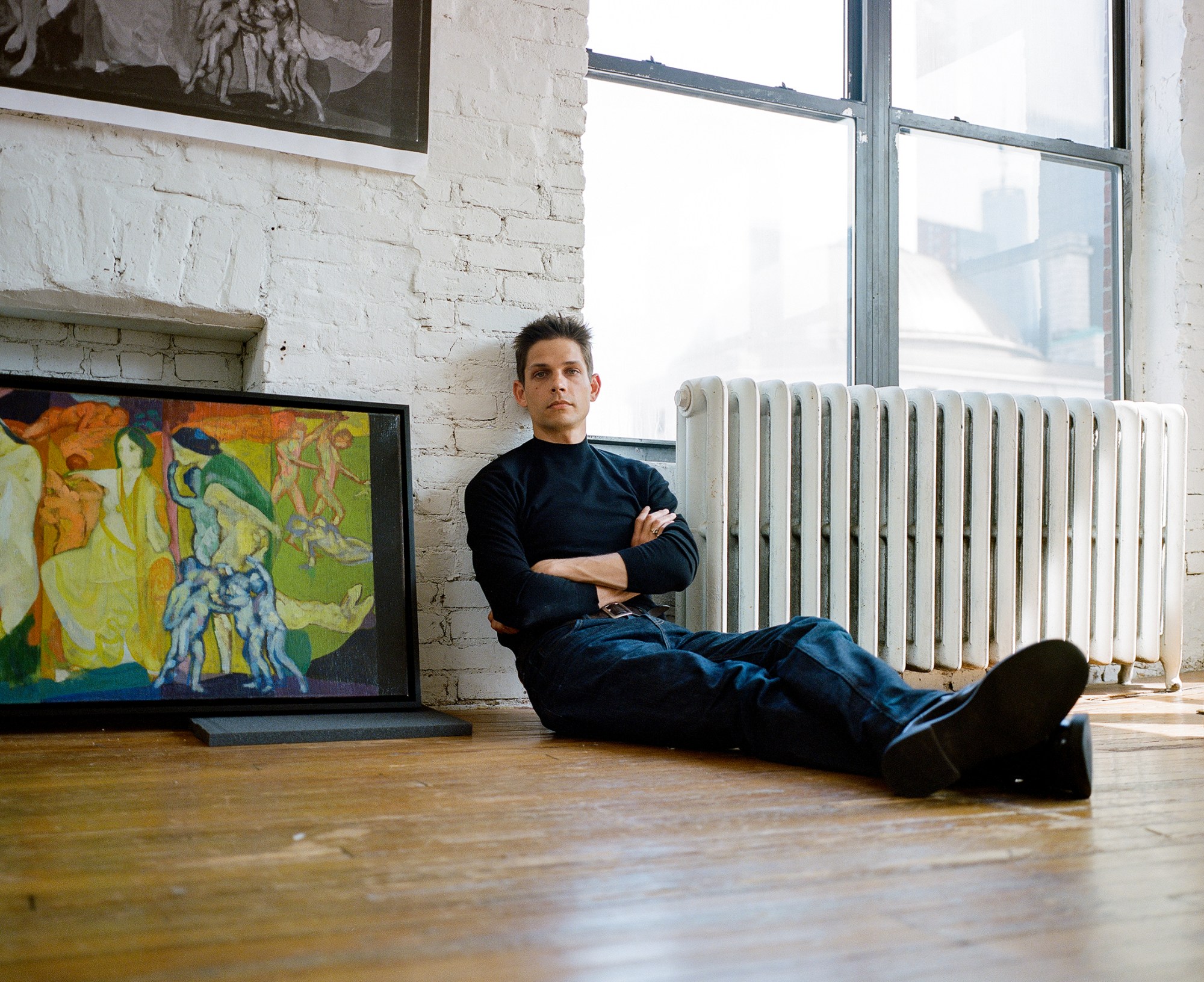 ethan james green sitting next to a green and orange painting at his gallery