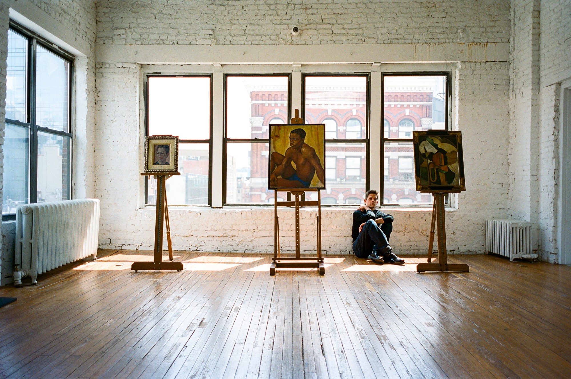 ethan james green sitting behind three paintings at his gallery