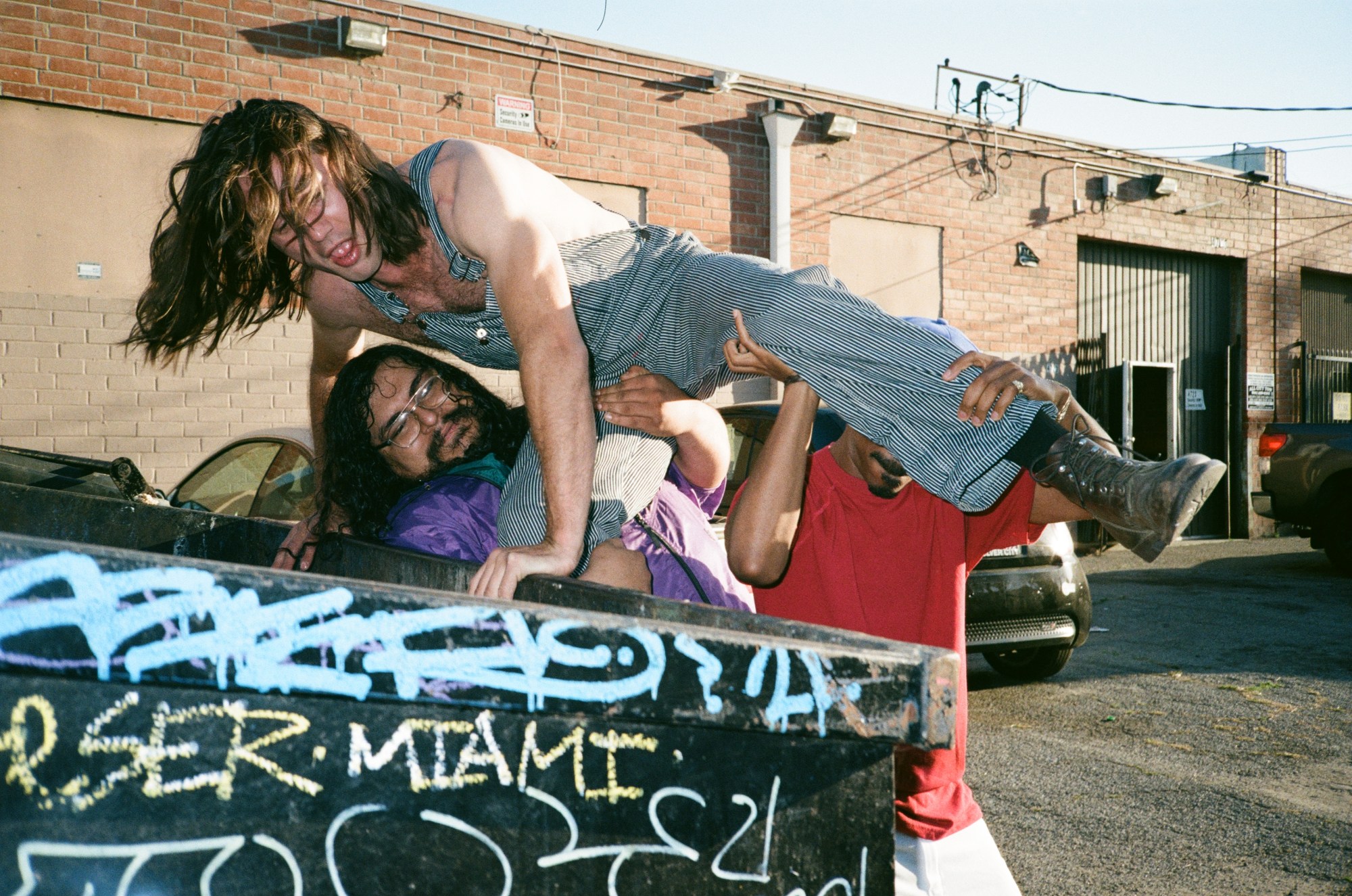 two men throw another man into a dumpster