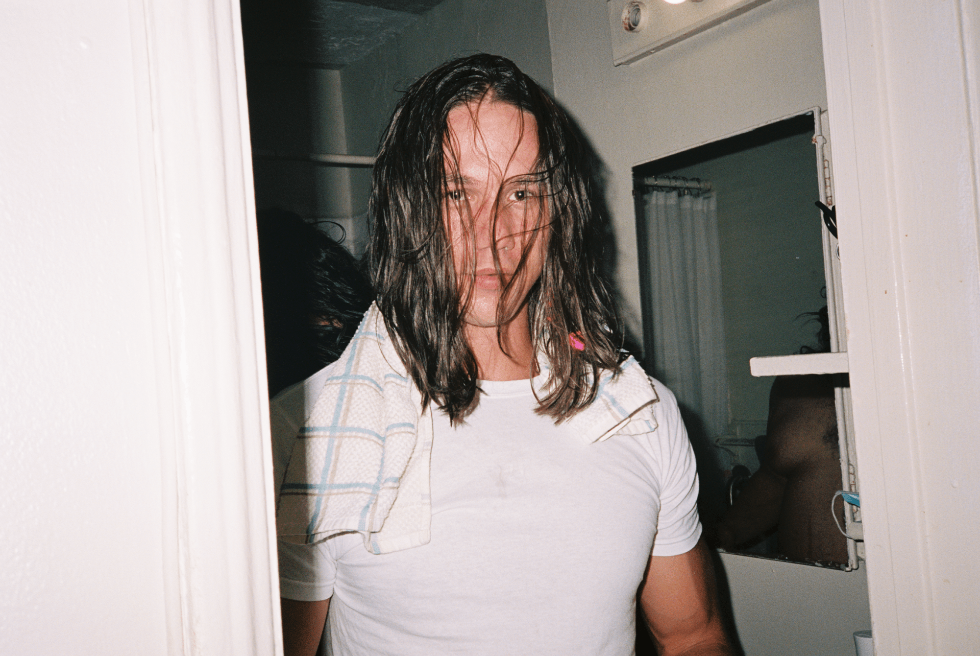 a man with long hair wearing a white t-shirt with a towel draped over his shoulders