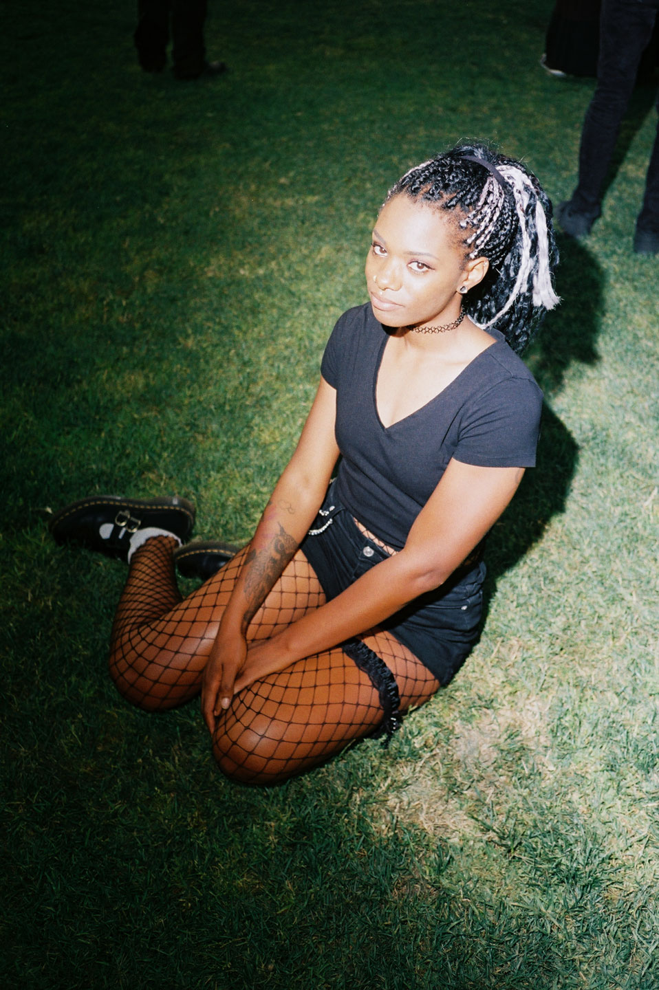 a goth girl wearing black denim hotpants with fishnets and docs sits in the grass