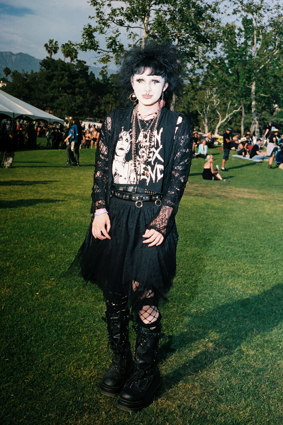 a goth wearing big black boots, a tutu and an iggy pop shirt paired with messy black hair and cartoonish makeup