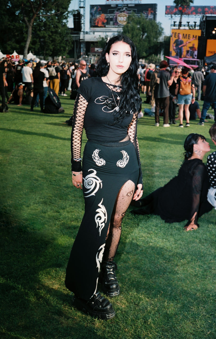 a goth girl wears big boots and an all-black fishnet-heavy look as she poses at a festival