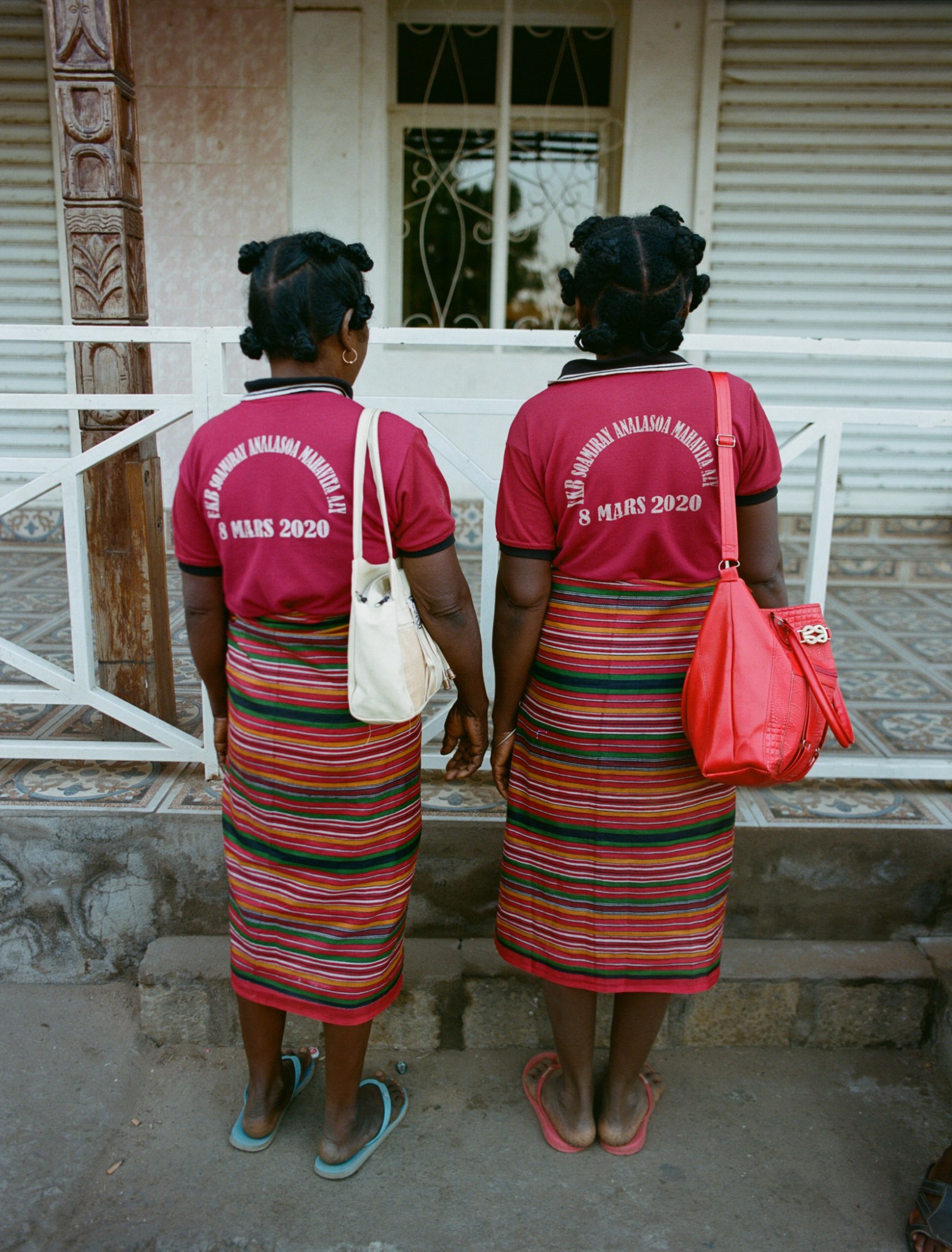 two women wearing bantu knots, red shirts, striped skirts and flip flops